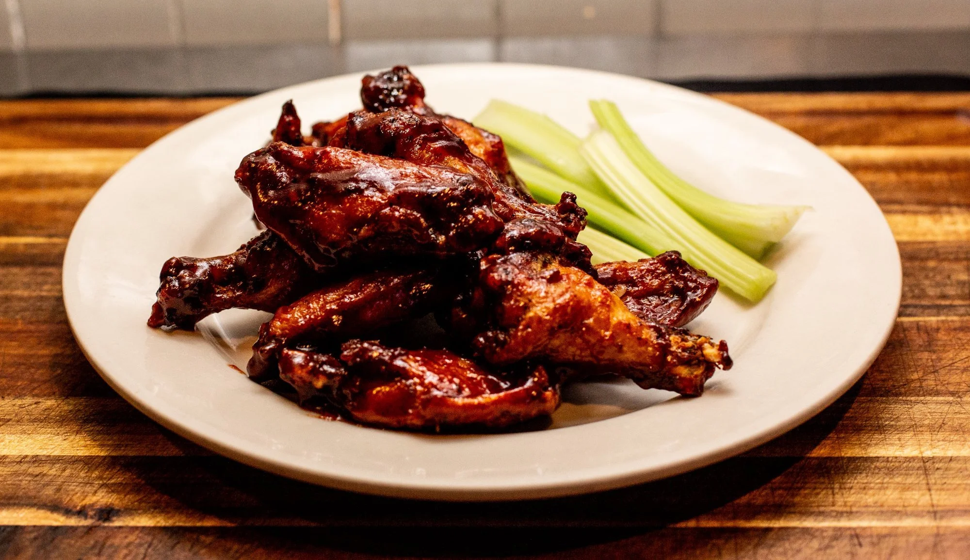 Plate of glazed chicken wings with celery sticks on a wooden surface.