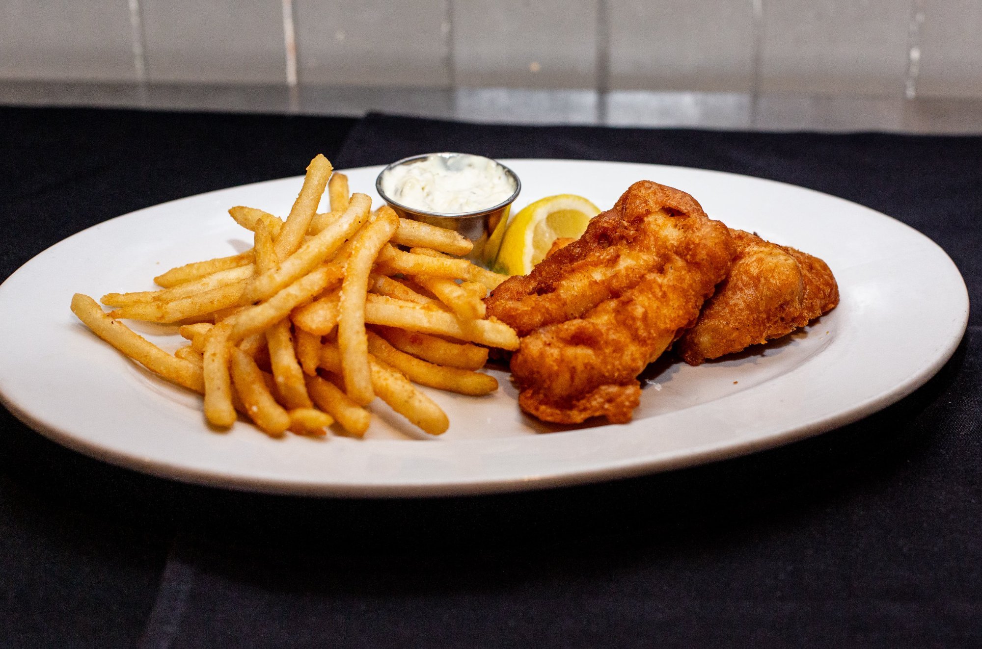 Fried fish fillets with French fries, lemon wedge, and tartar sauce served on a white plate.