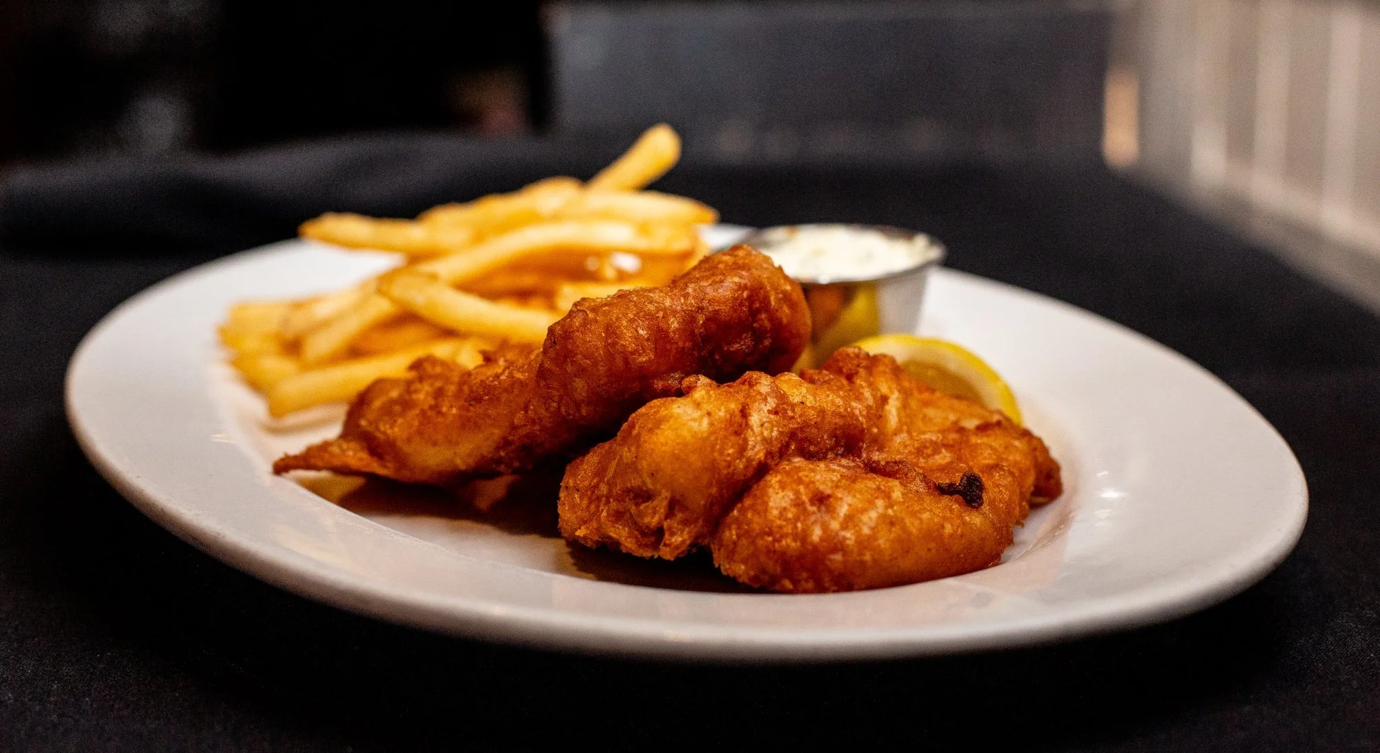 Plate of French fries and battered fried fish fillets with lemon wedges and dipping sauce.