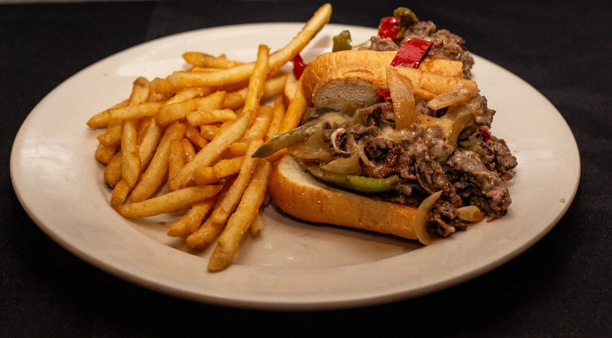 Philly cheesesteak sandwich with French fries on a white plate