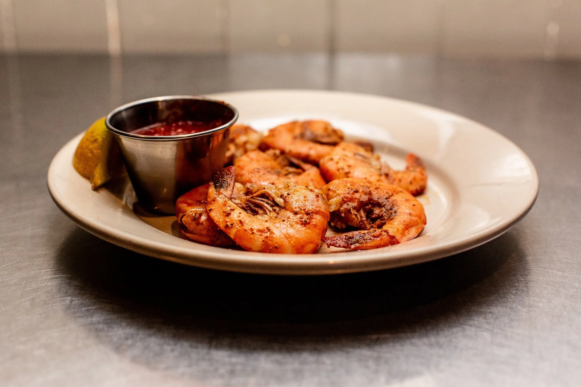A plate of cooked shrimp with a lemon wedge and a side of cranberry sauce in a small metal container.