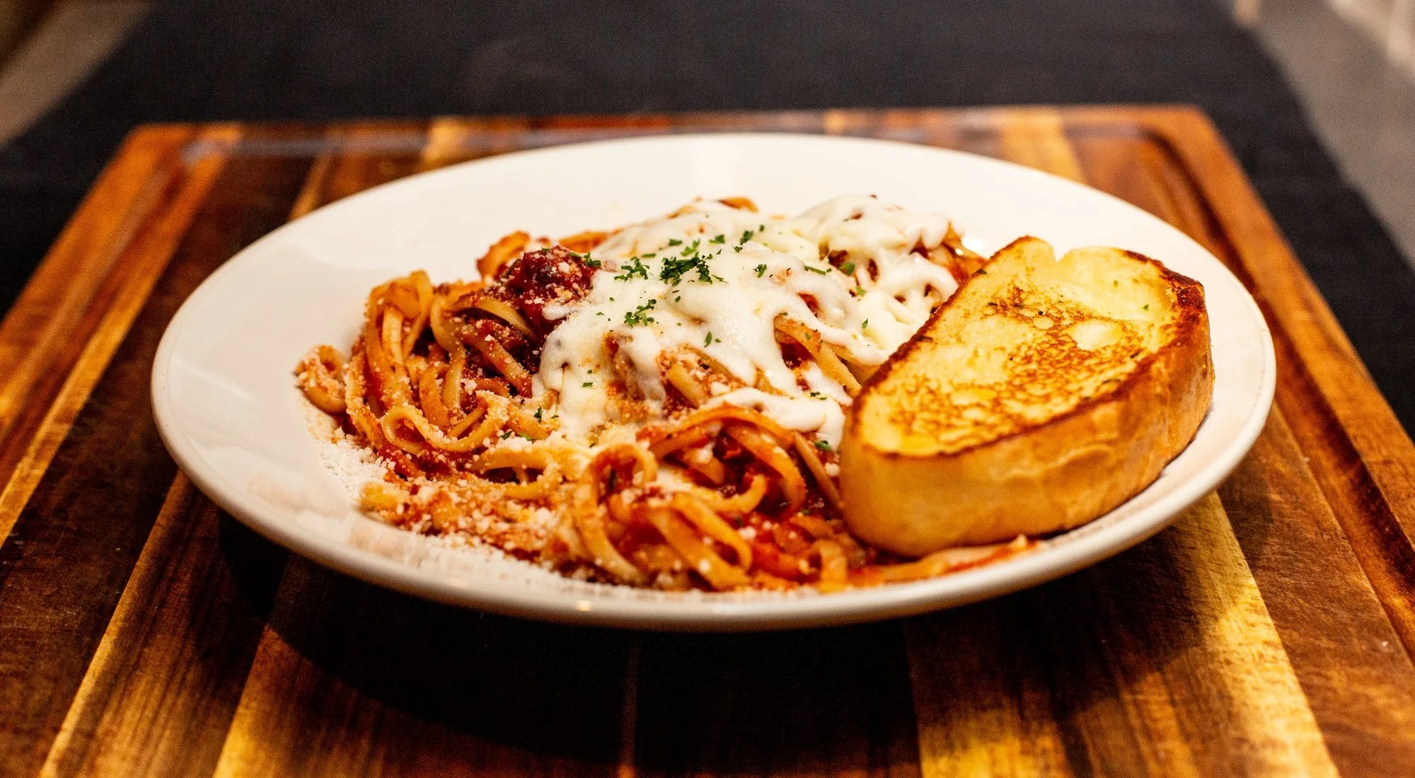 Plate of spaghetti with marinara sauce, topped with melted cheese and parsley, served with a toasted garlic bread on a white dish.