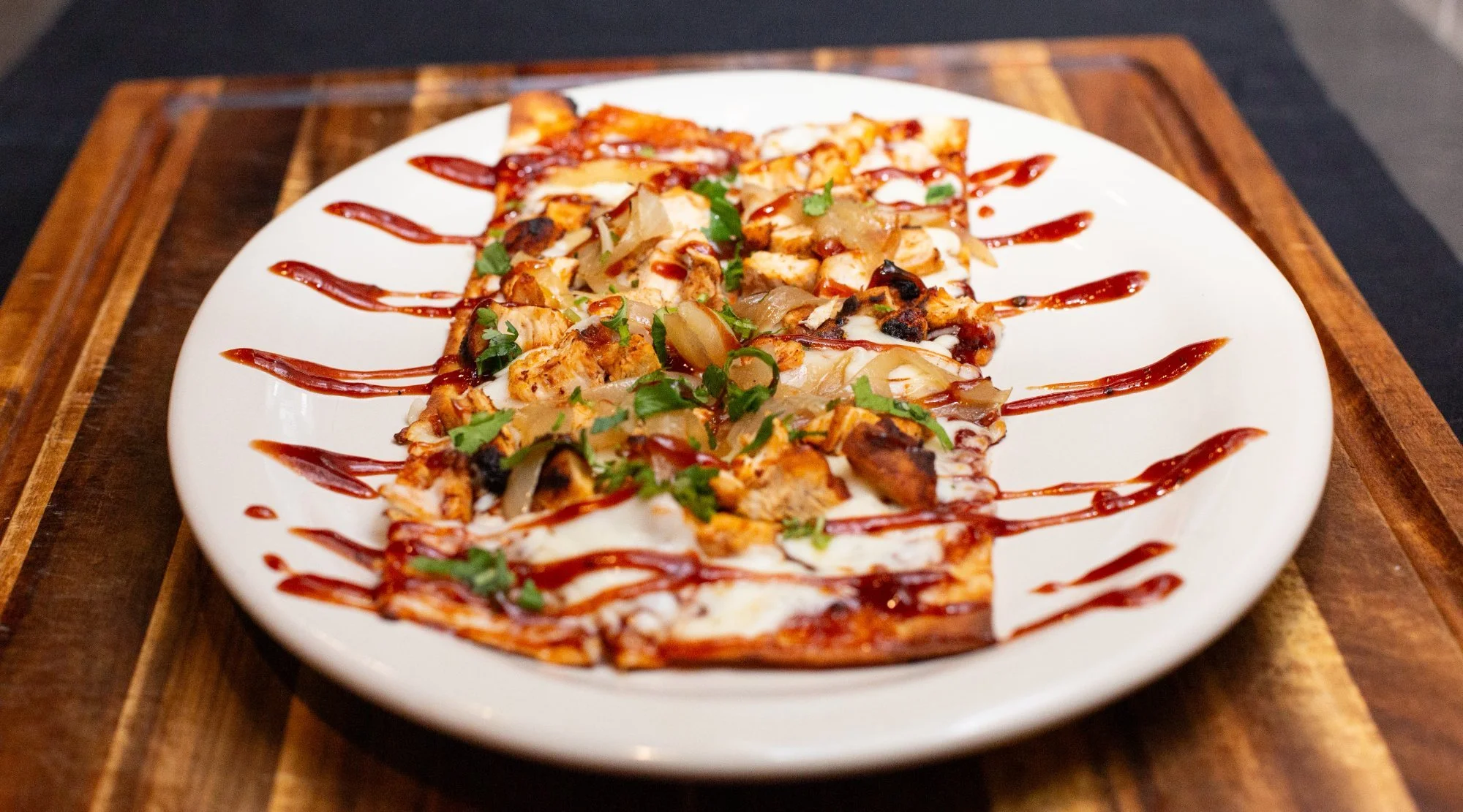 A plate of flatbread pizza topped with chicken, cheese, onions, cilantro, and drizzled with ketchup.