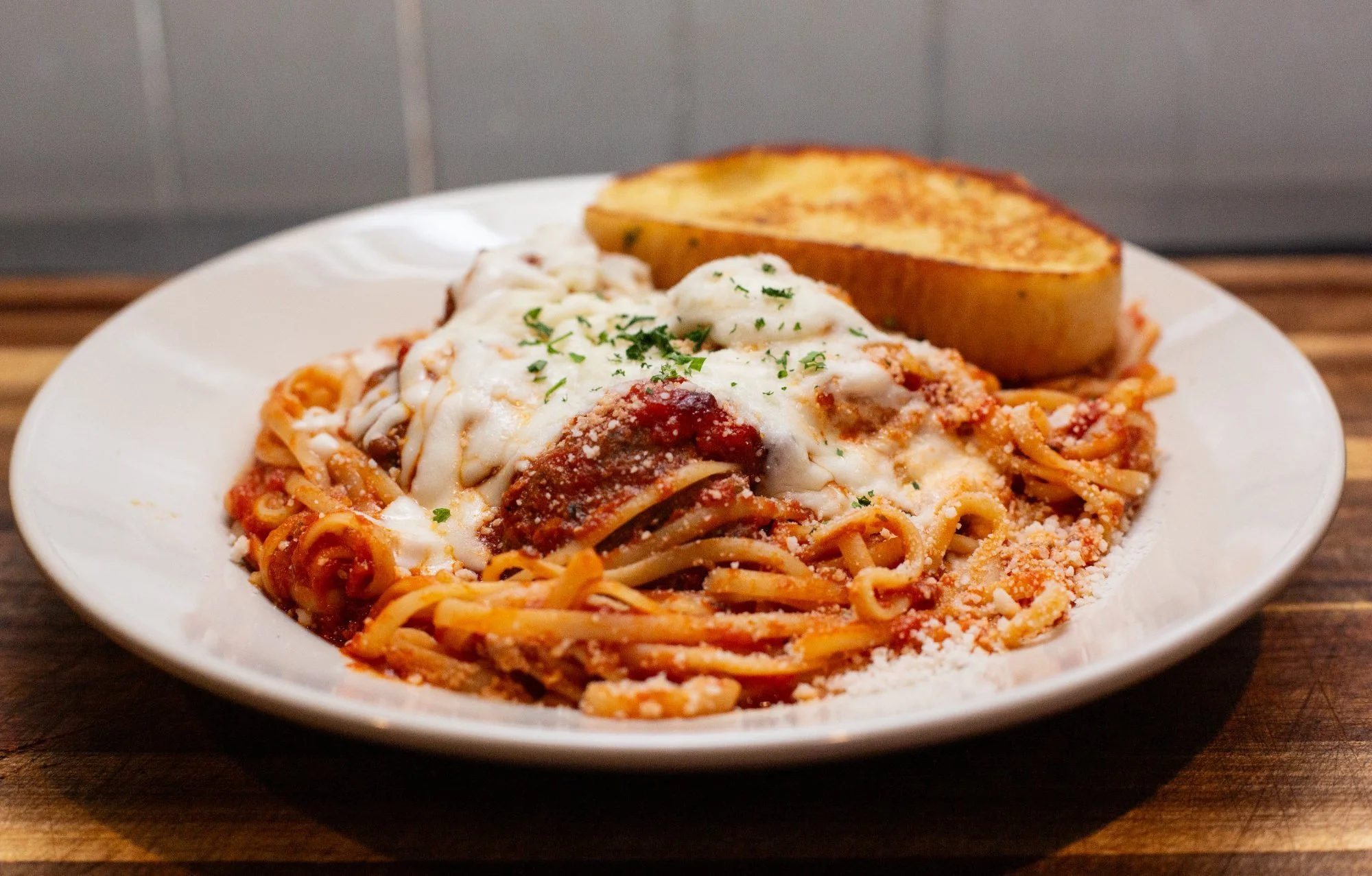 Plate of linguini with marinara sauce topped with melted cheese and chopped parsley, served with a baked potato.