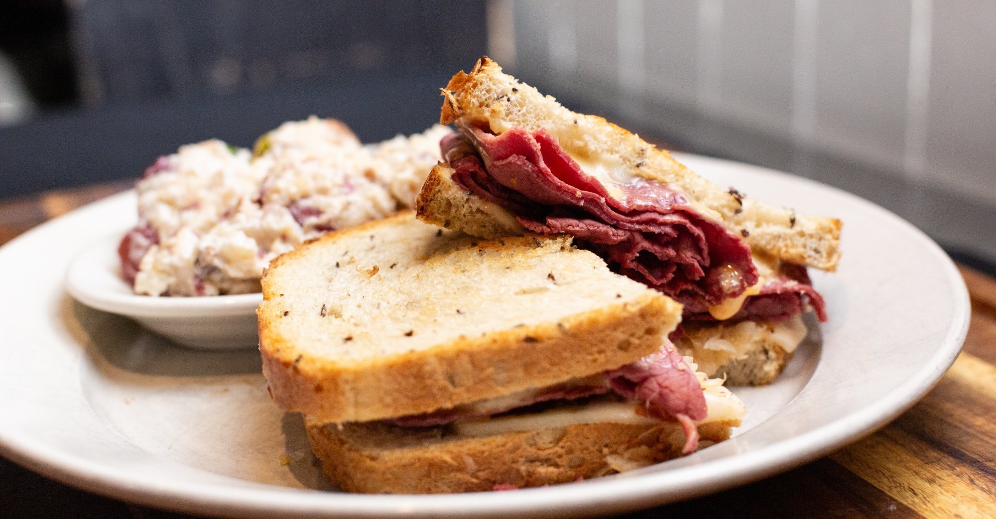 A plate with a sliced roast beef sandwich on toasted bread and a side of potato salad.