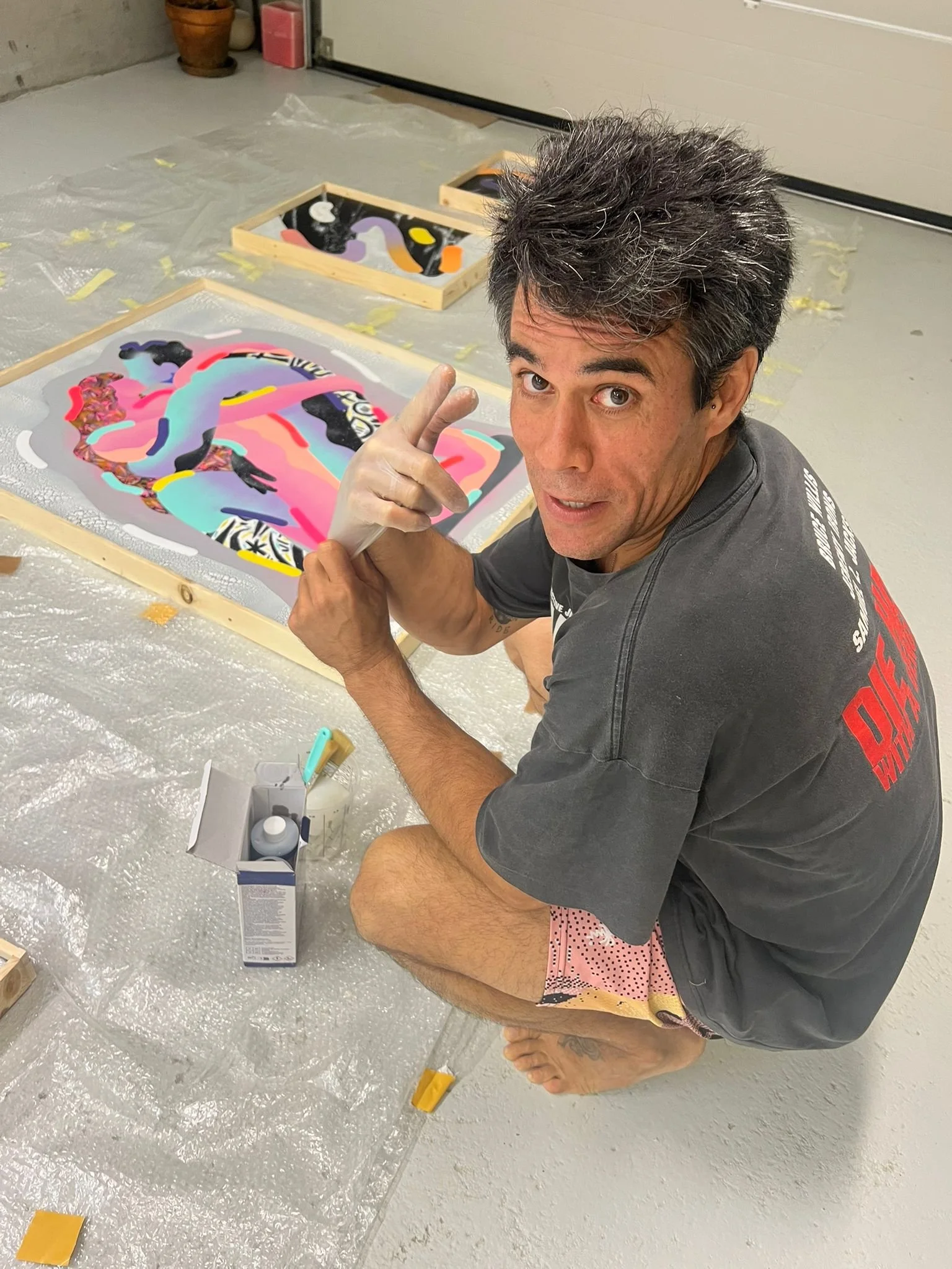 Javi Luque artista haciendo arte de estilo Pablo Picasso con pintura en acrílico en un lienzo, en una habitación con piso de cemento, utilizando pintura en varios colores y lienzos sobre el suelo.