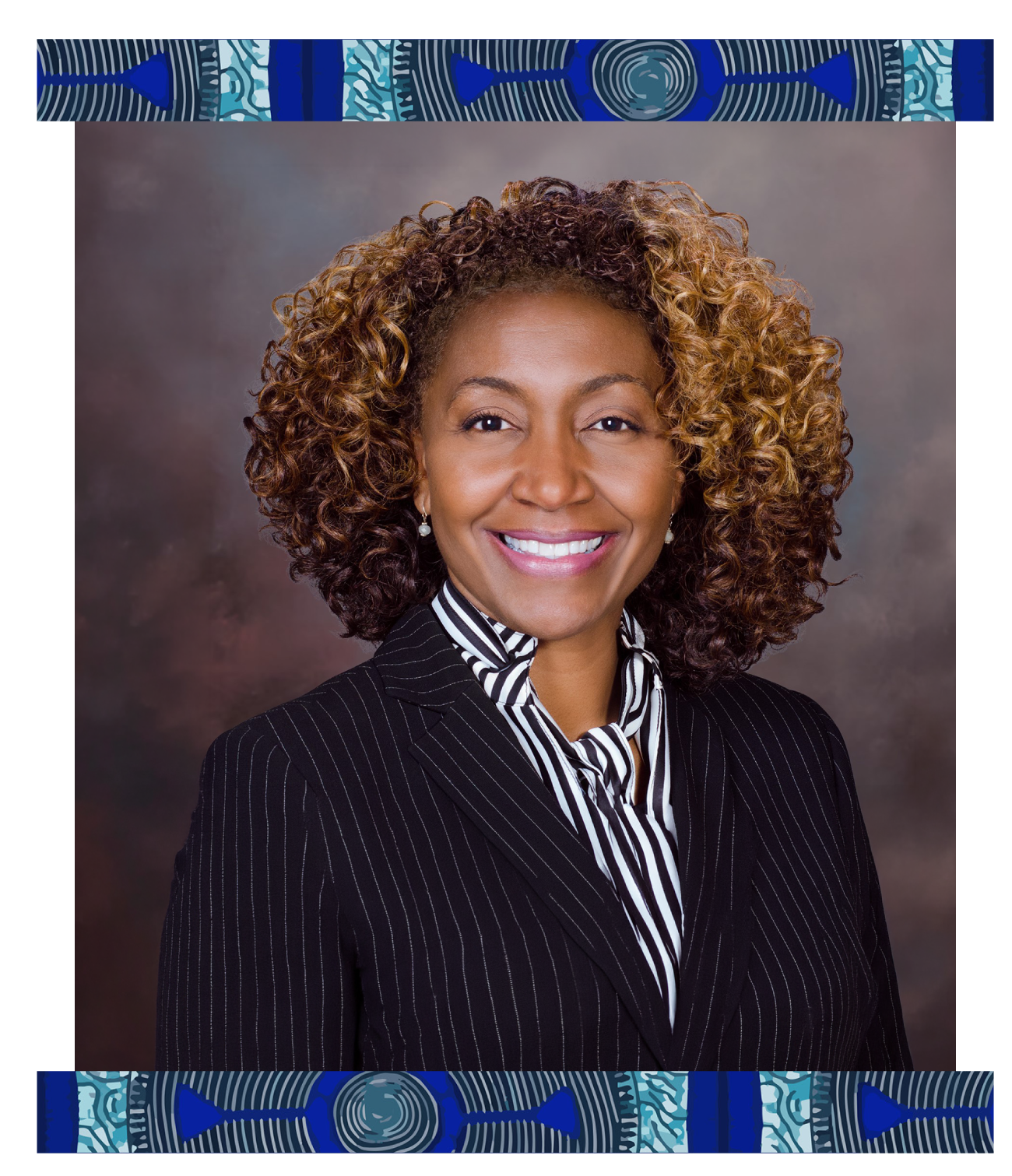 A professional woman with curly hair smiling and wearing a pinstripe blazer and a striped shirt, posed against a neutral gray background.