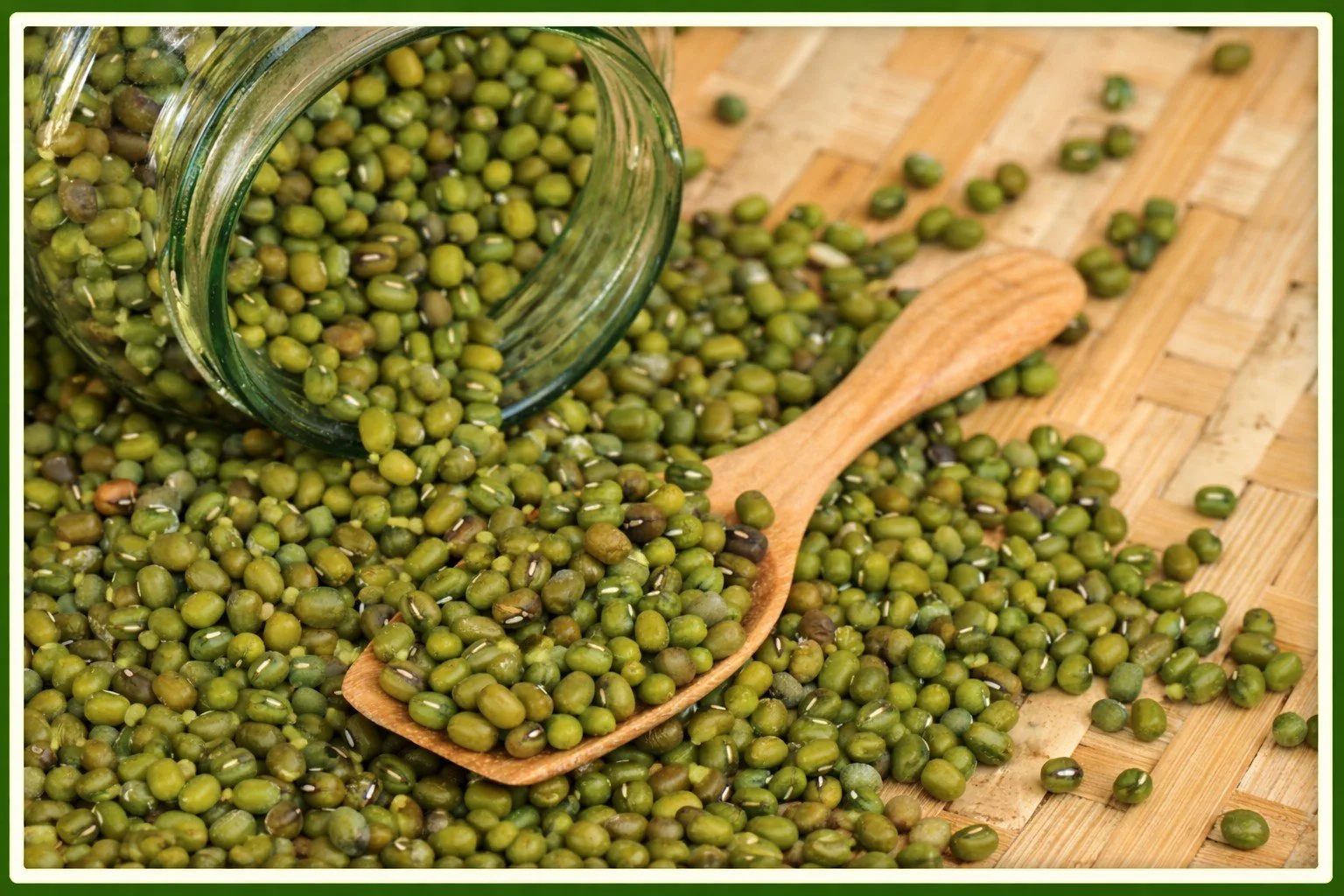 Green mung beans spilling from a glass jar onto a table surface,