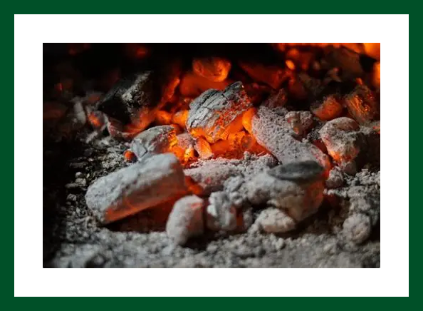 Glowing red and orange embers among gray ashed charcoal.