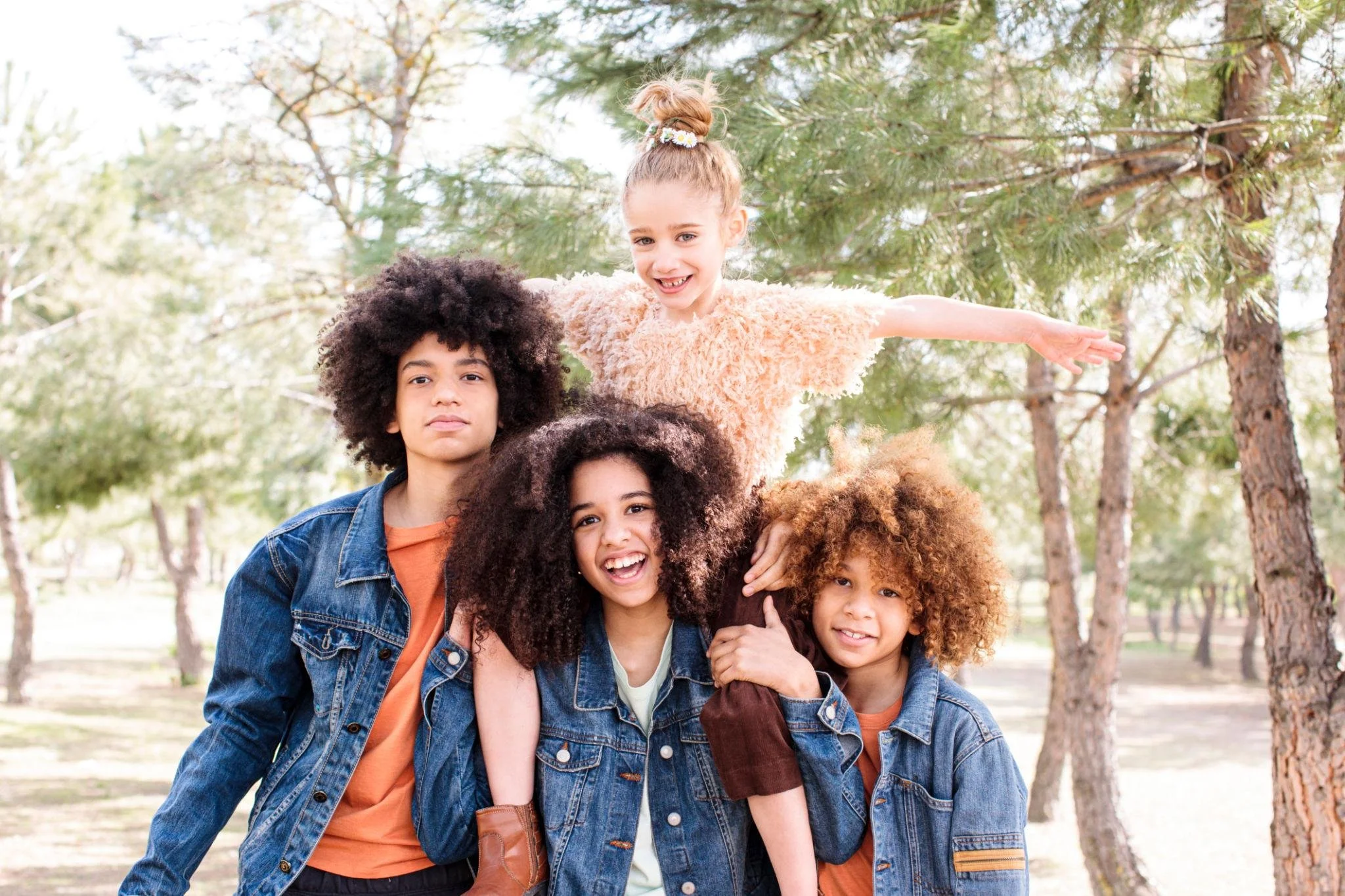 Group of five diverse children outdoors in a park, standing close together, smiling, with trees in the background.