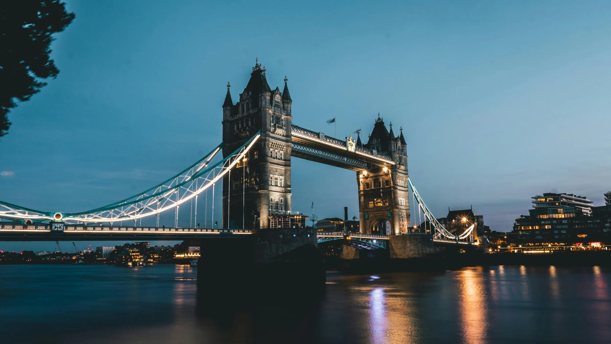 London Tower Bridge illuminated at dusk over the River Thames with city lights reflecting on the water.