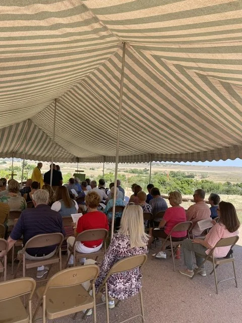 Parishioners, family, and friends gather for an outdoor service. 