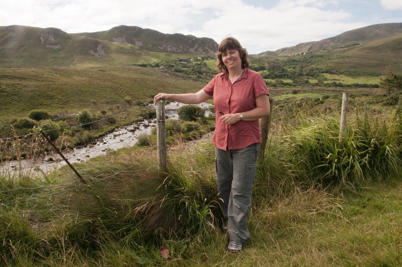 Linda Detwiler Burner standing in a scenic mountain landscape during her travels