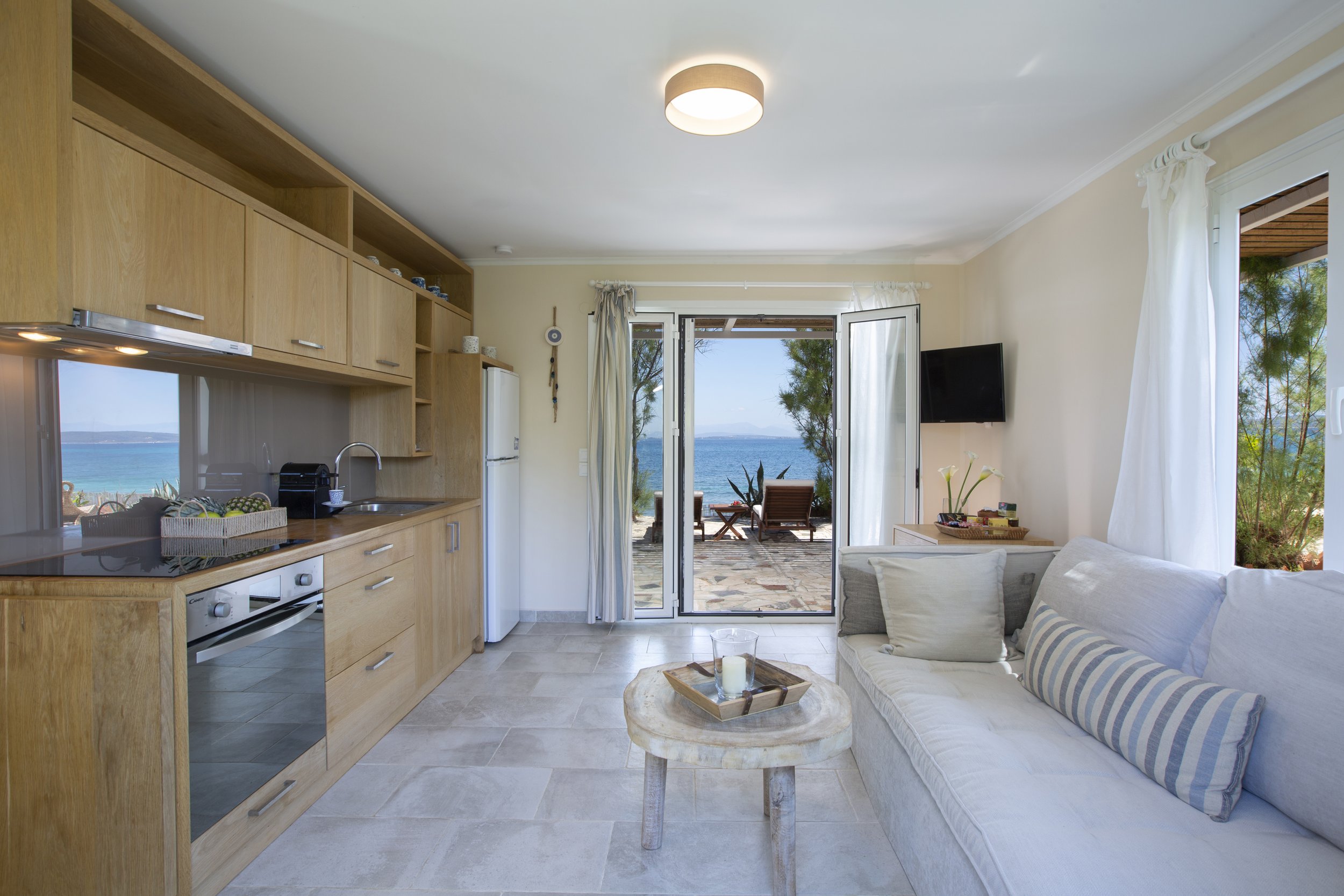 A cozy living room with sliding glass doors leading to a patio with outdoor chairs and a view of the ocean and sky.