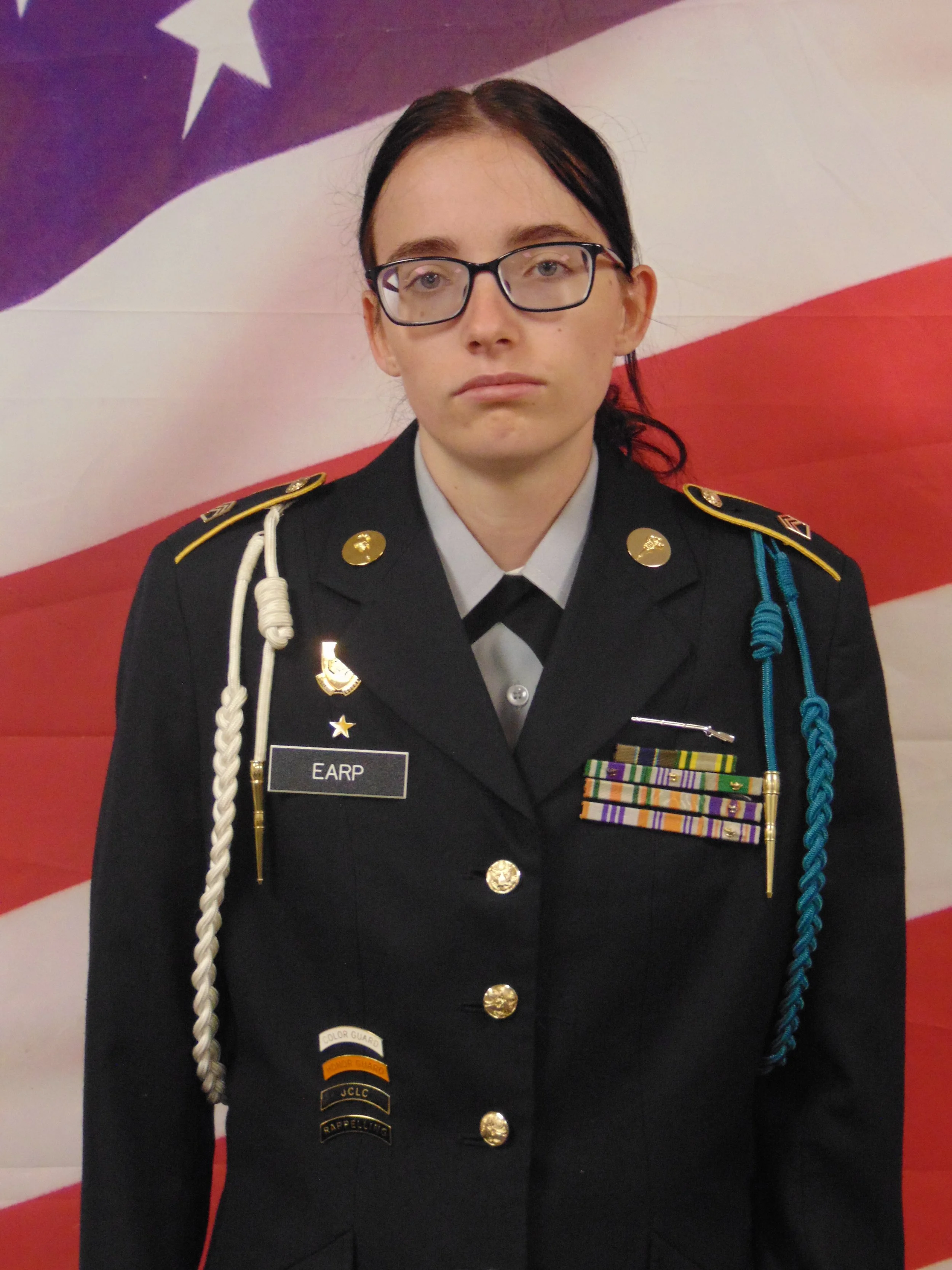 A woman in a military uniform standing in front of an American flag.