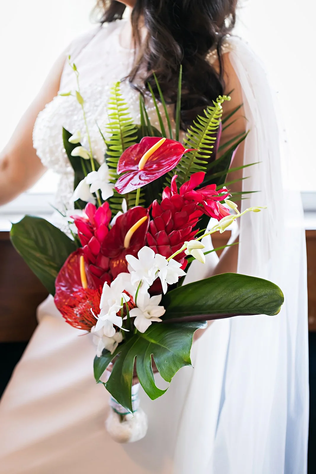 A bride in a white dress holding a tropical bridal bouquet of red, white, and pink tropical flowers with green foliage on Yacht Starship in Tampa, Florida. Photo by Limelight Photography
