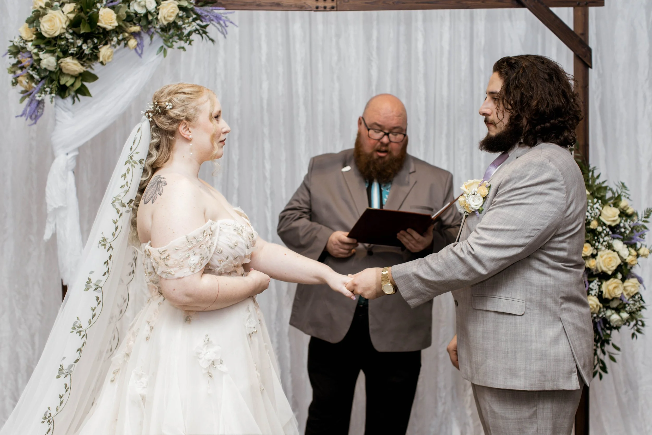 Couple holding hands during wedding ceremony with floral arch photo courtesy of Heather Rosario Photography