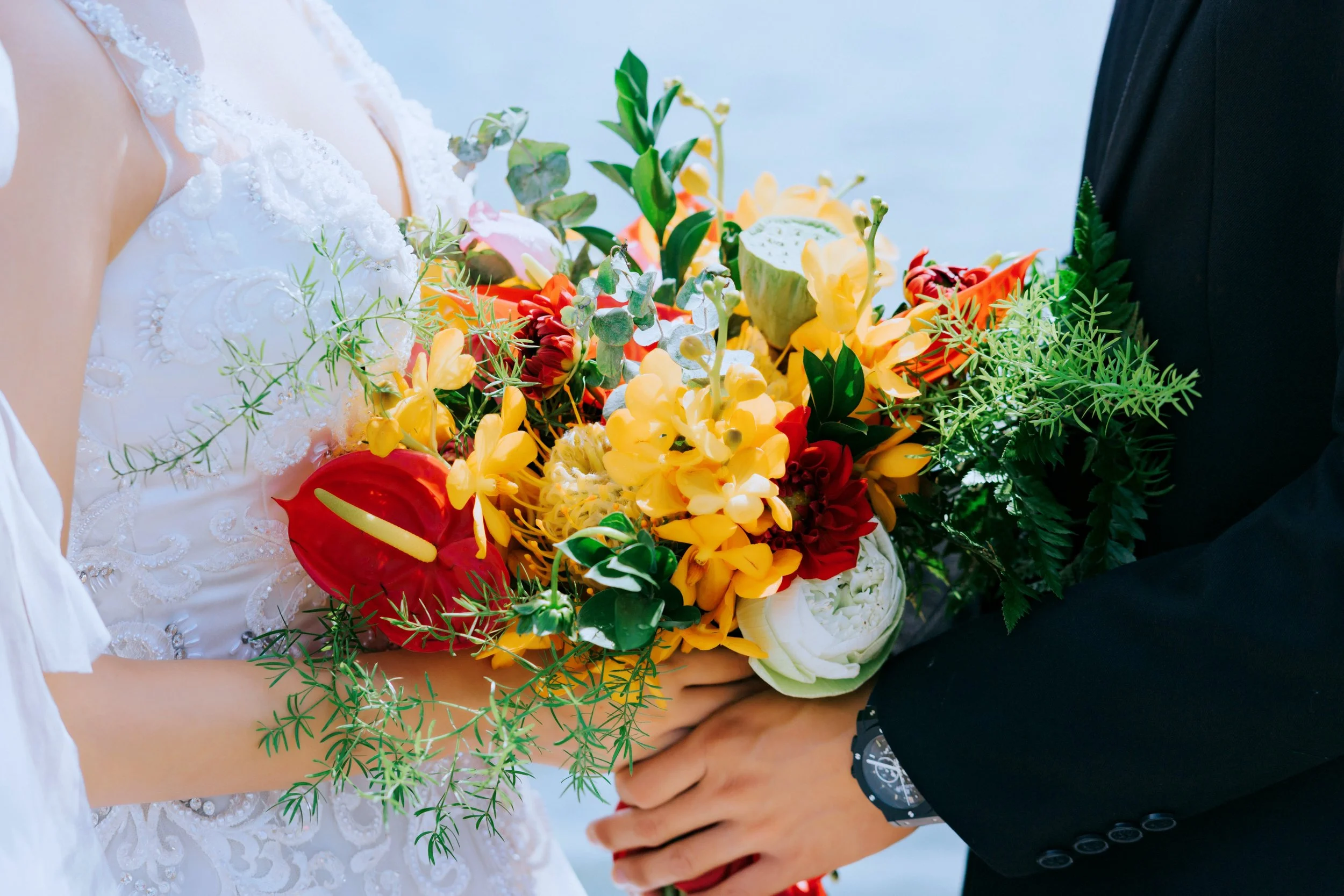 Close-up of a bride and groom holding a colorful bouquet of flowers during a wedding ceremony, with the bride wearing a white dress and the groom in a dark suit.