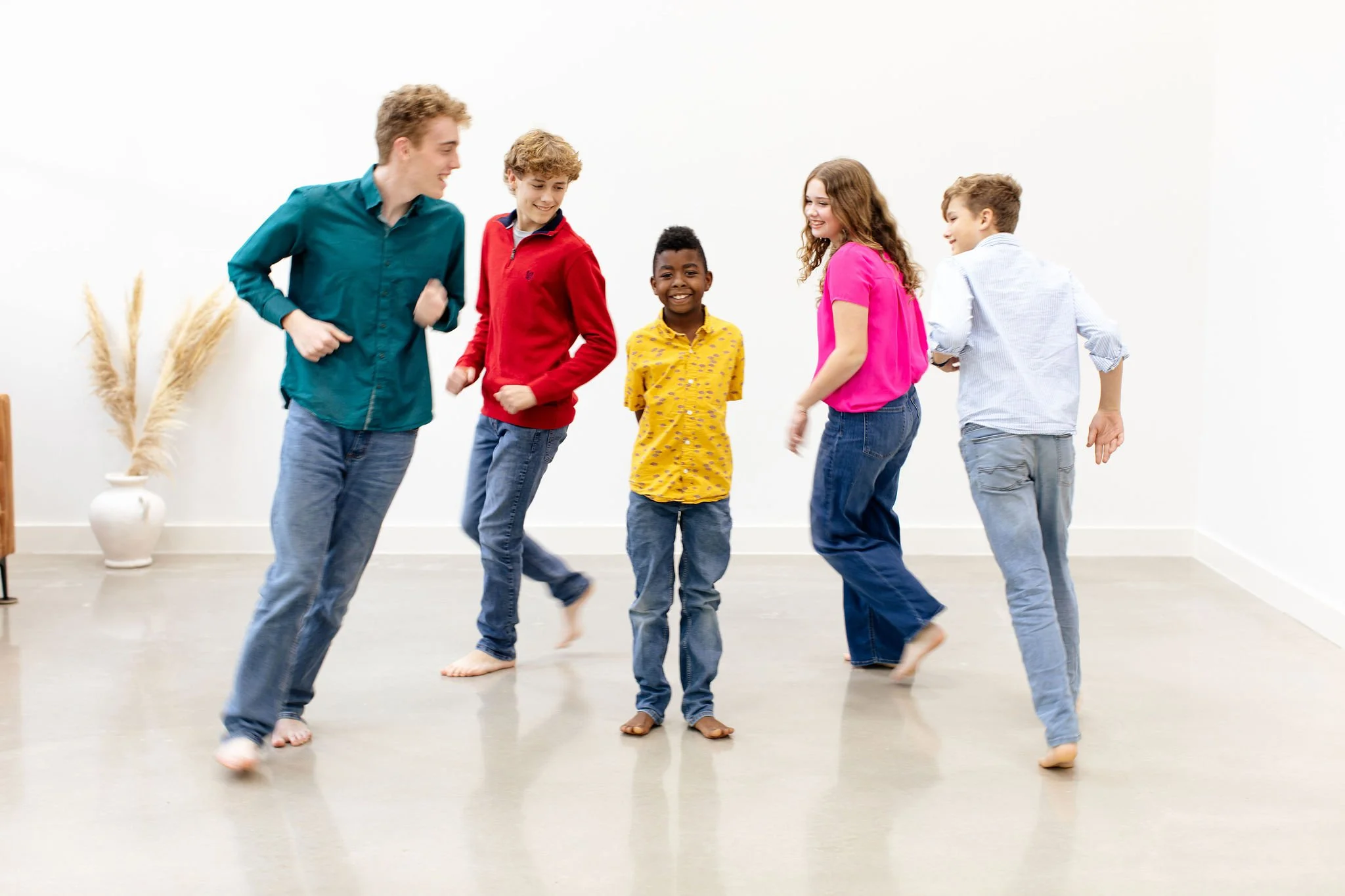 Group of six children dancing and smiling in a bright, minimalistic room.