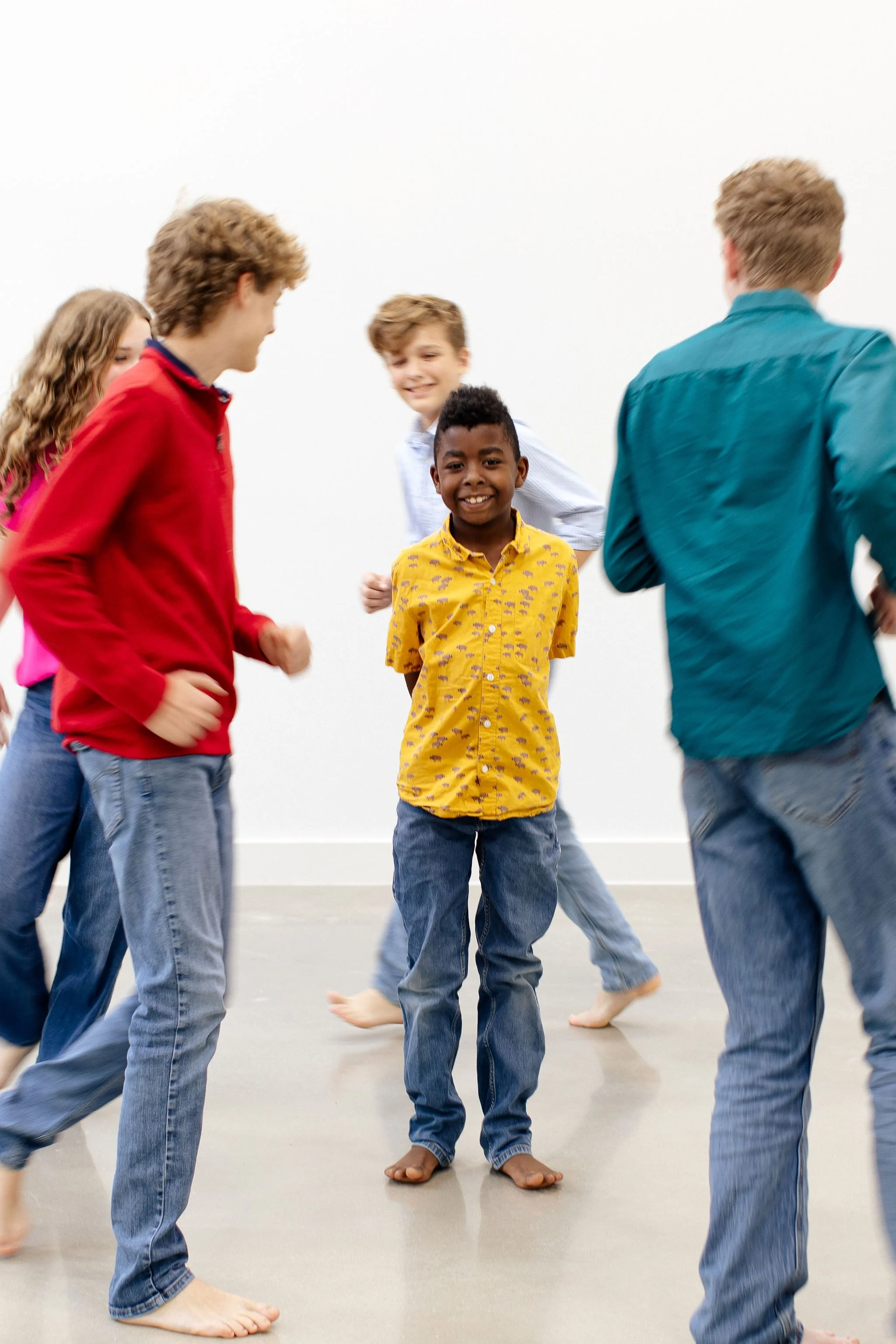 A group of children playing together barefoot indoors, smiling and engaging in an activity.