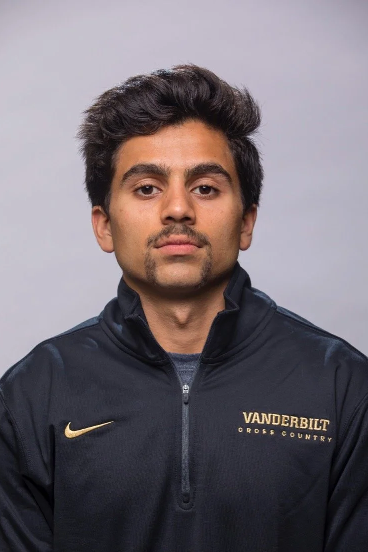 A man wearing a black Vanderbilt Cross Country jacket with a gold Nike logo, posing against a plain gray background.