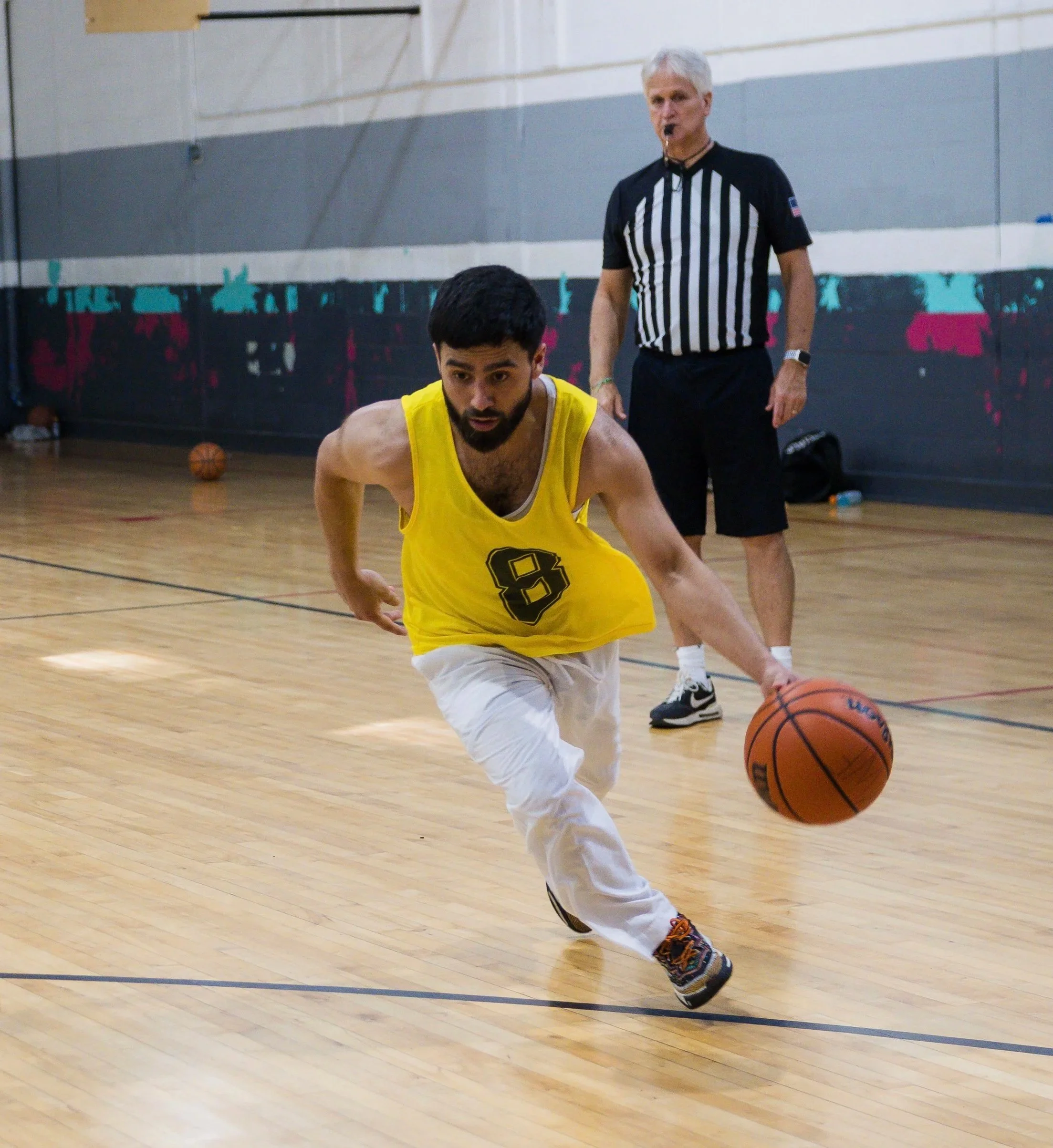 A man in a yellow basketball jersey with the number 8, dribbling a basketball on an indoor court, with a referee in the background.