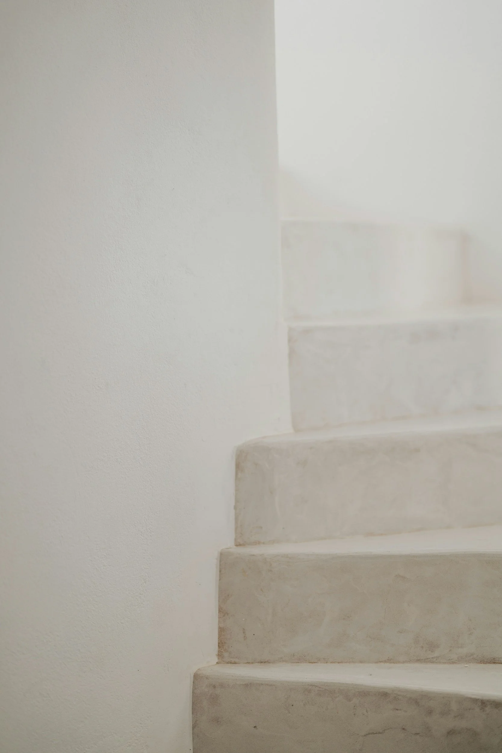 A close-up of a marble staircase with four steps, white walls on either side, and a textured wall surface.