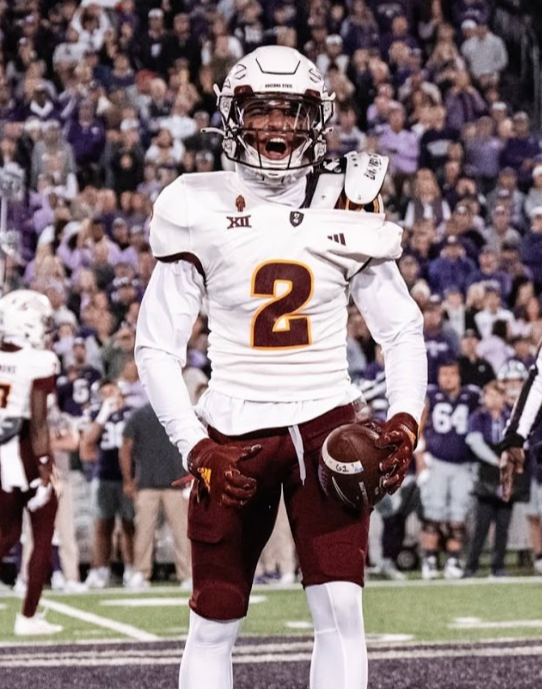 A football player in a white jersey with the number 2, wearing a helmet and gloves, standing on the field during a game with a crowd in the background.