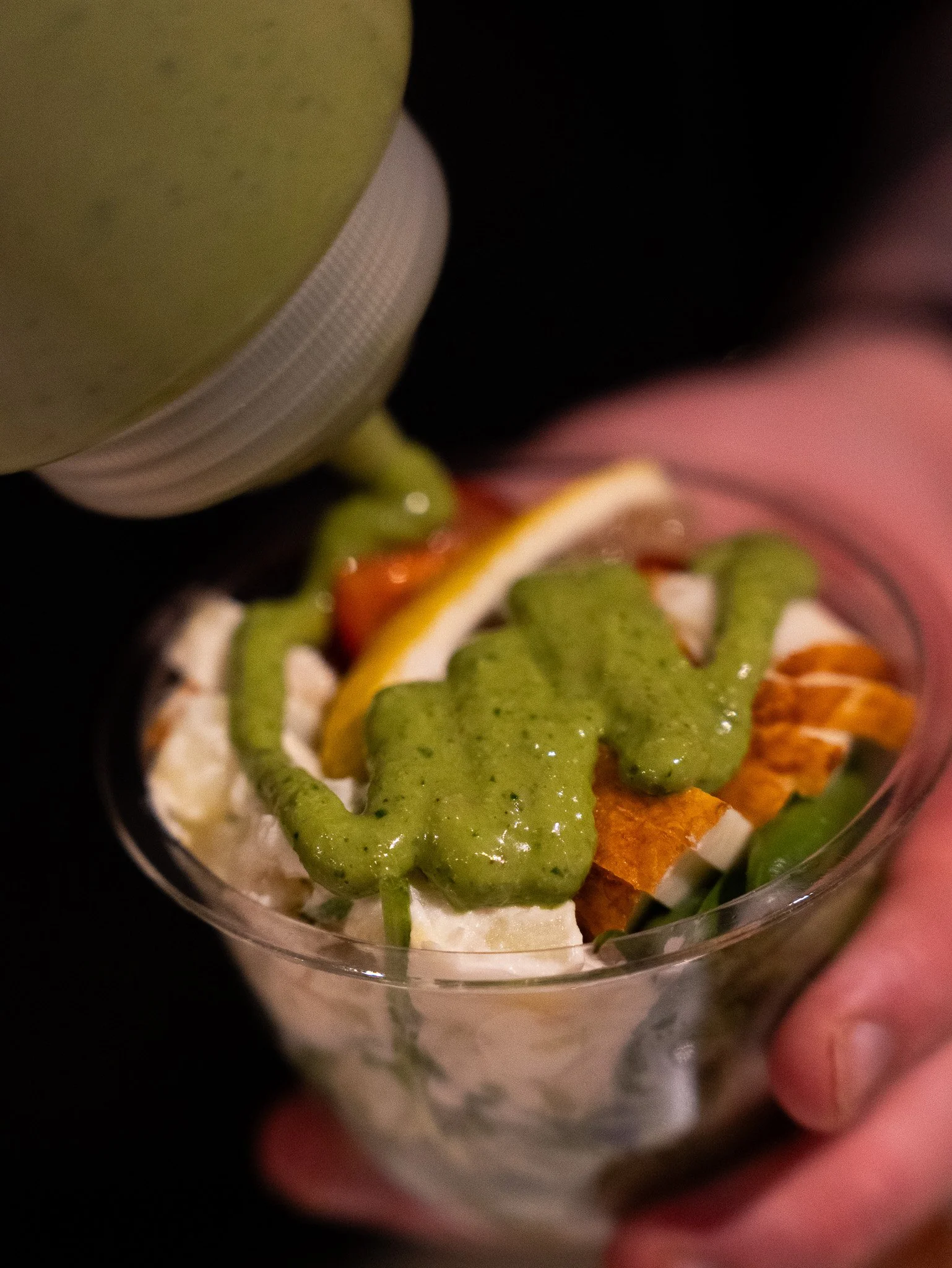 A small glass of salad topped with green dressing, containing sliced lemon, cherry tomatoes, cucumbers, and other vegetables.