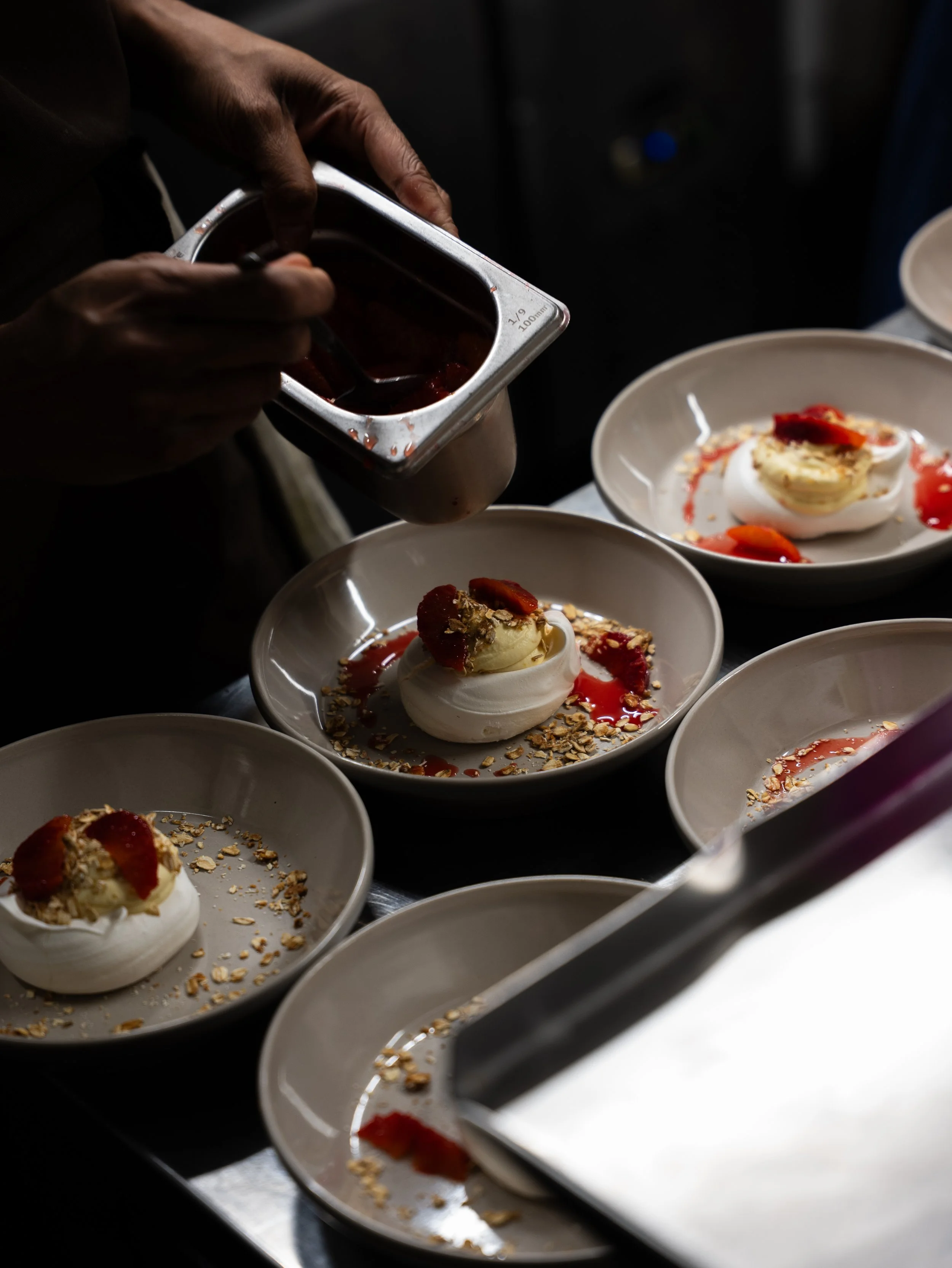 Chef decorating individual pavlova desserts with berry sauce and crushed nuts.