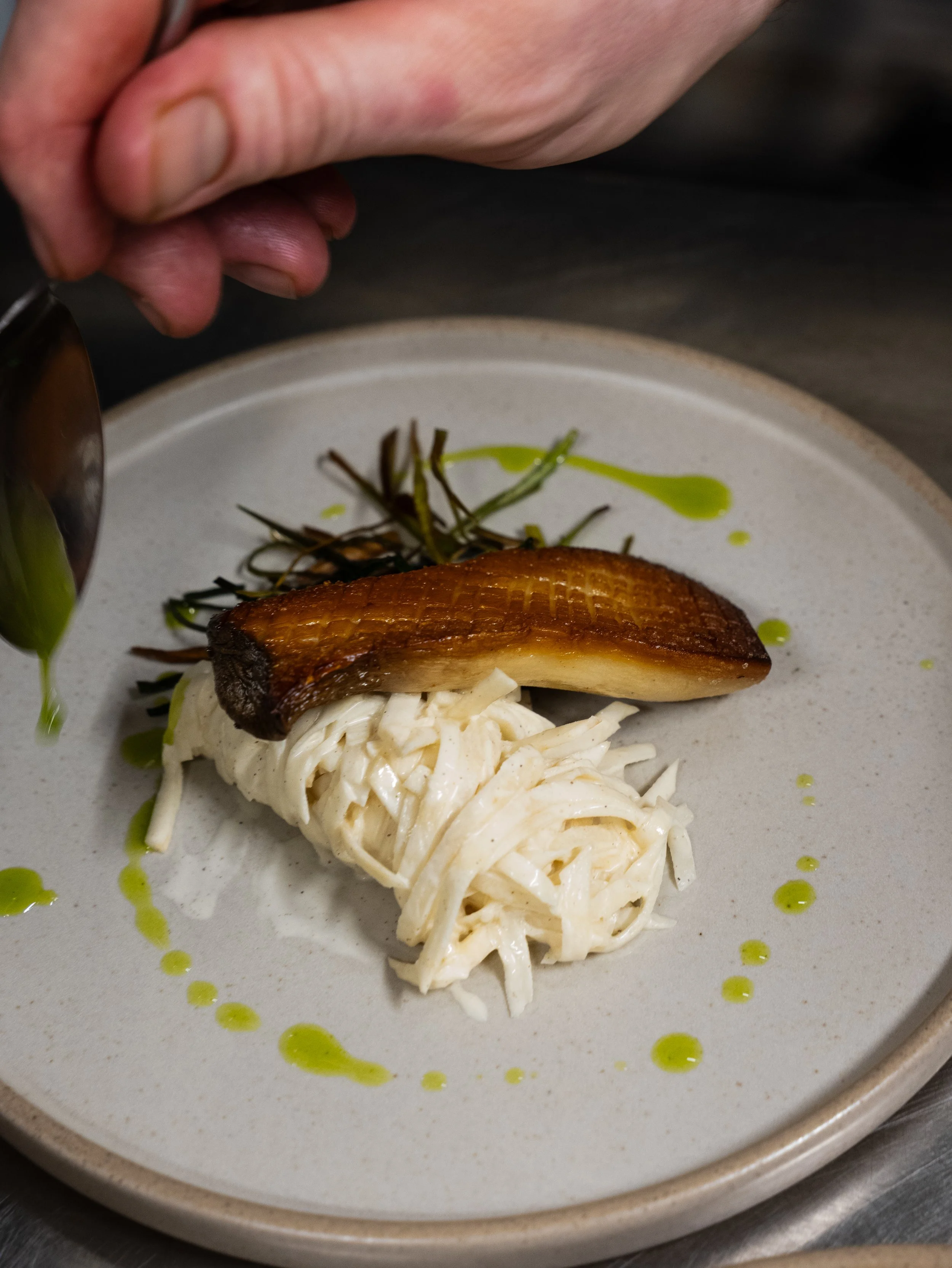 A plate of food with a piece of cooked fish placed on a bed of shredded vegetables, garnished with green sauces and herbs.