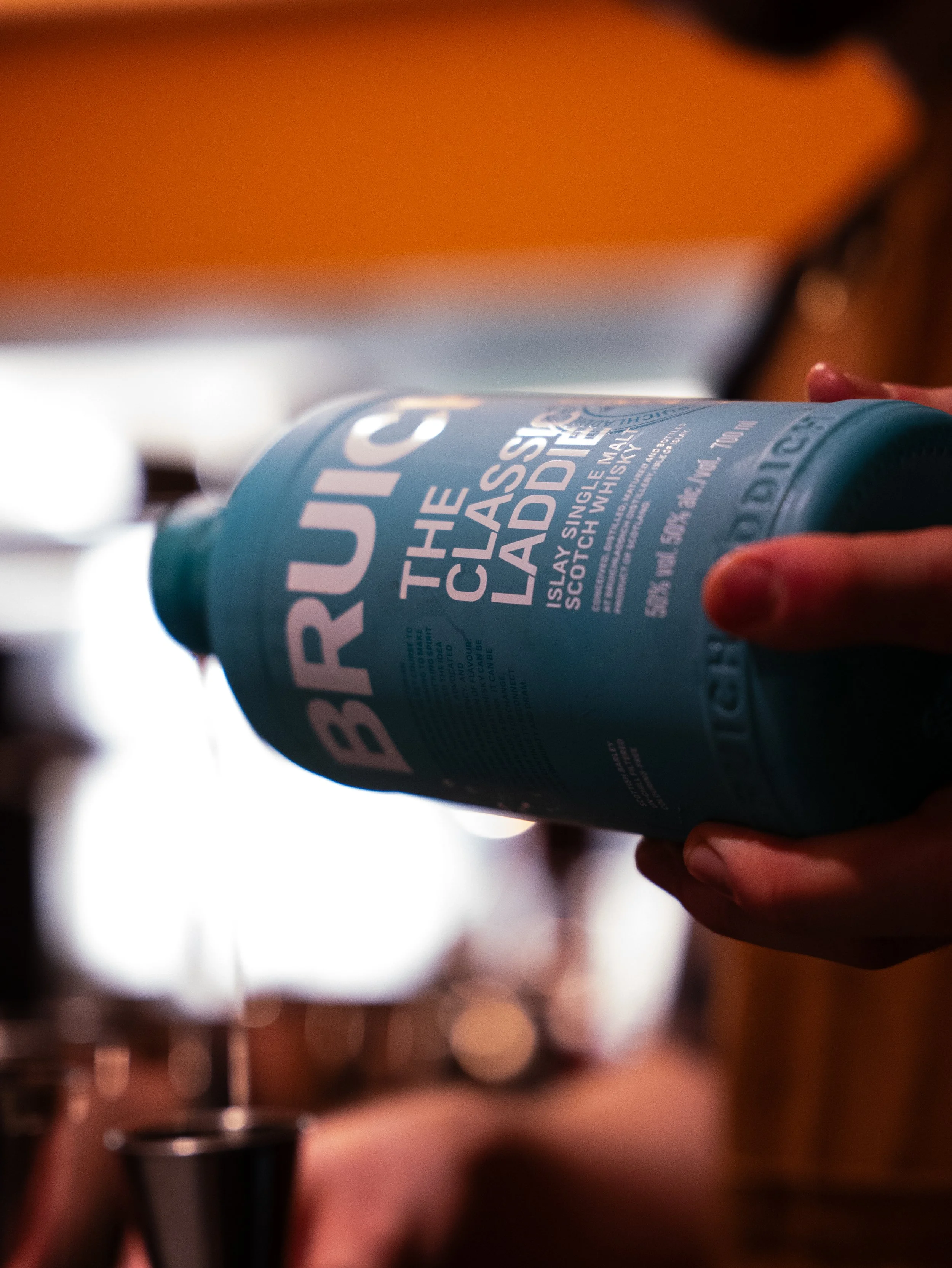 Close-up of a person pouring Bruichladdich classic Laddie single malt Scotch whisky from a teal bottle.