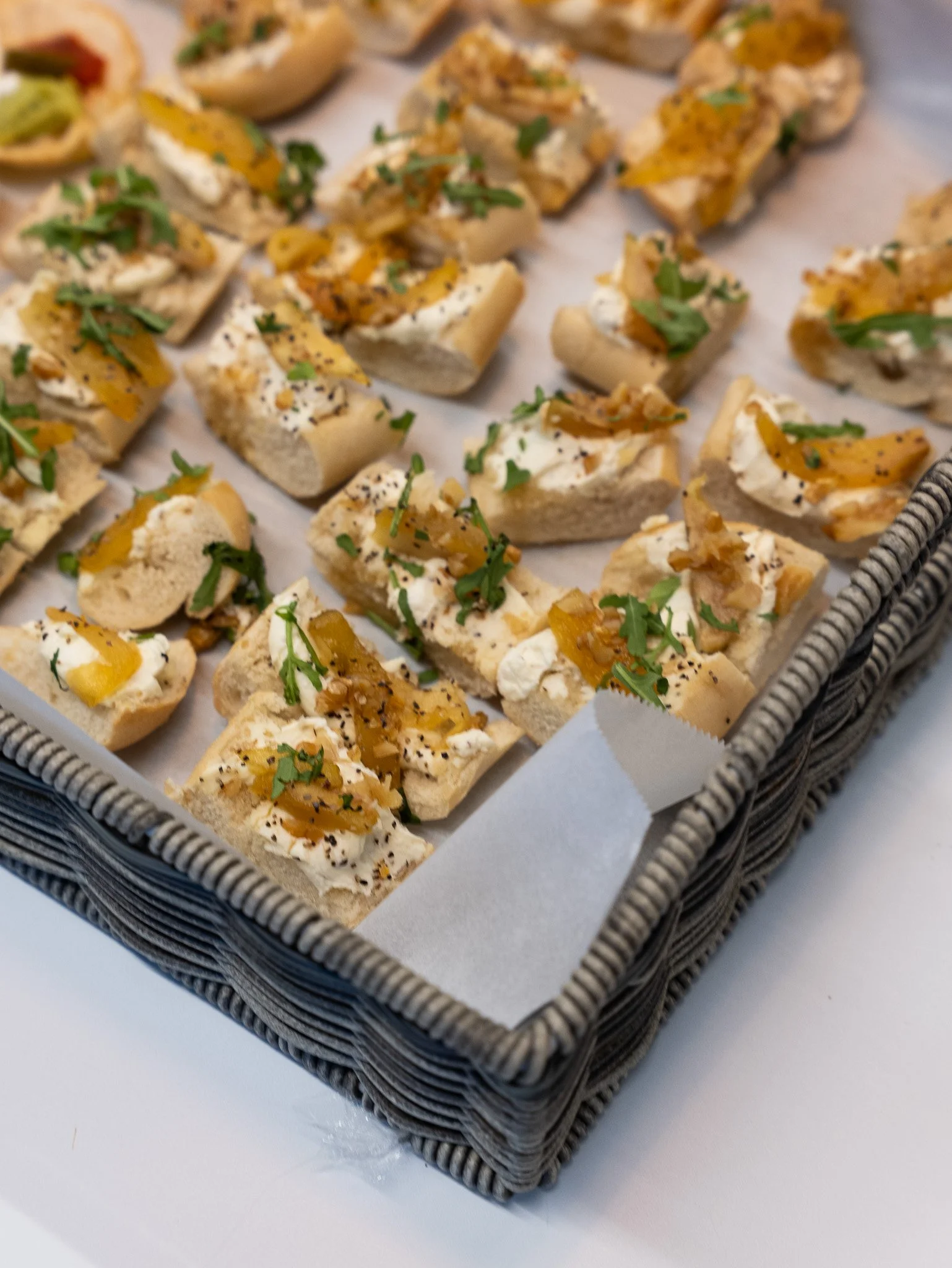 Tray of canapés with bread topped with cream cheese, caramelized onions, and herbs