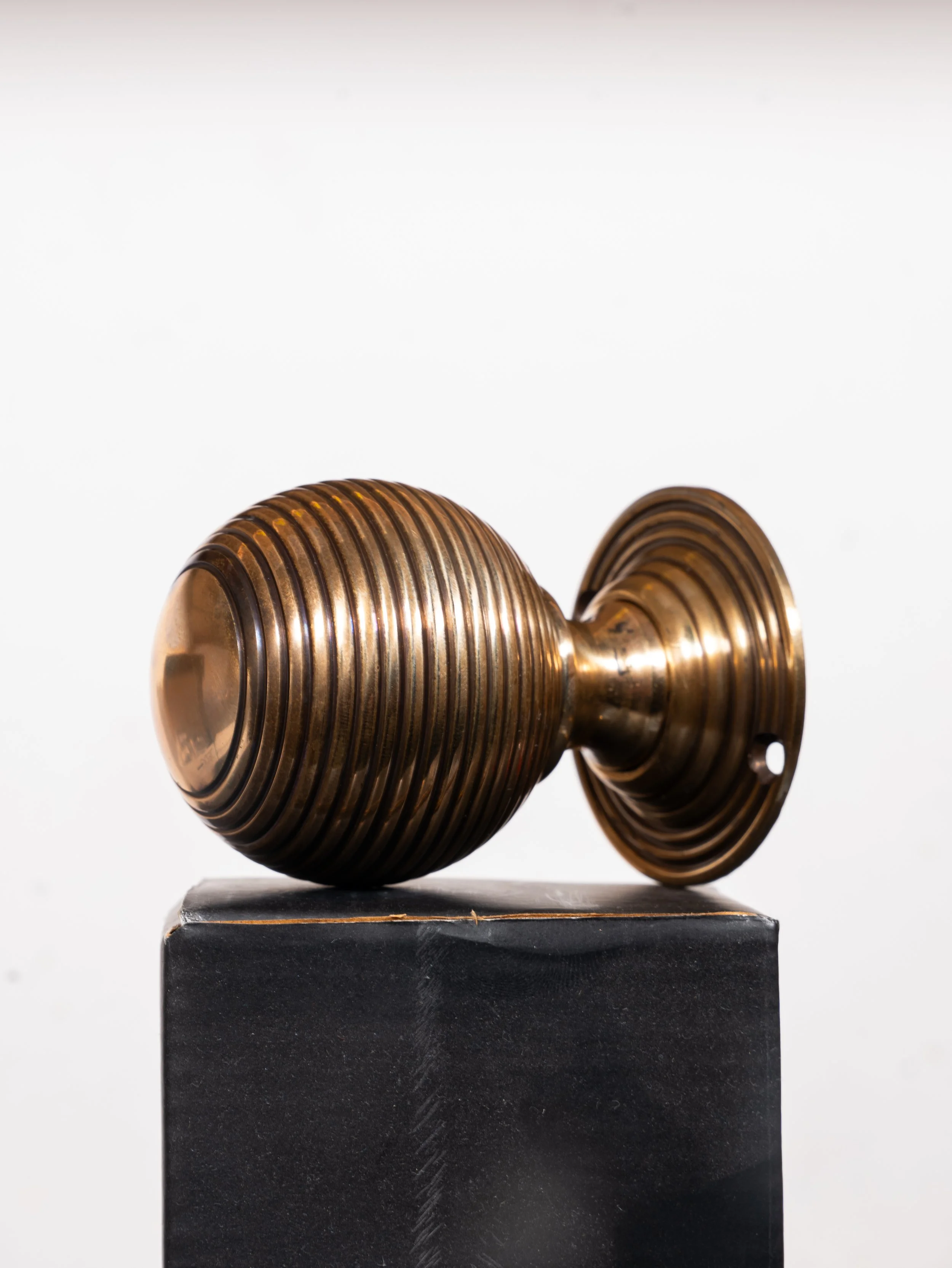 A vintage brass door knob with circular ridges on a black pedestal.