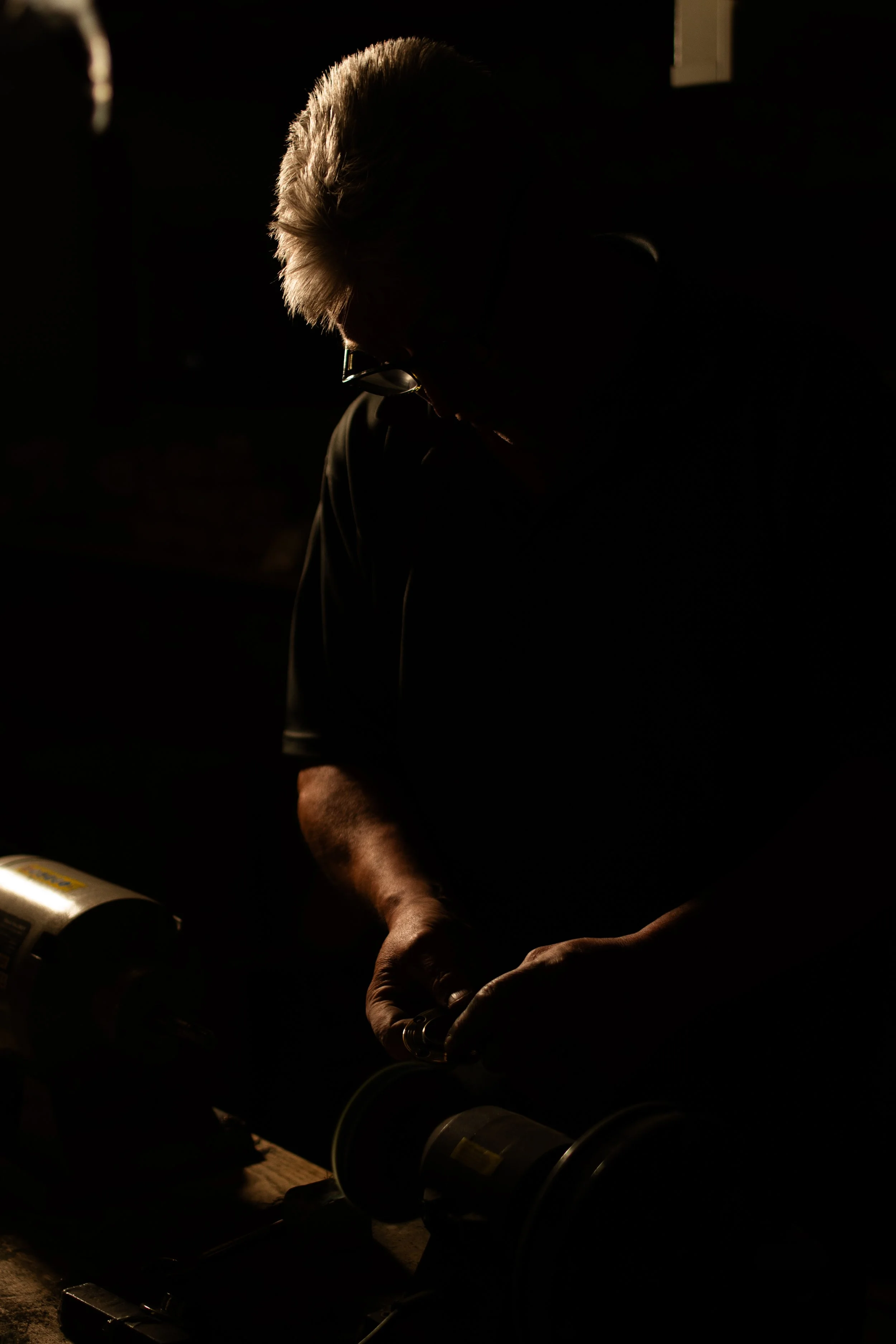 Silhouette of a person working with tools in a dimly lit environment.