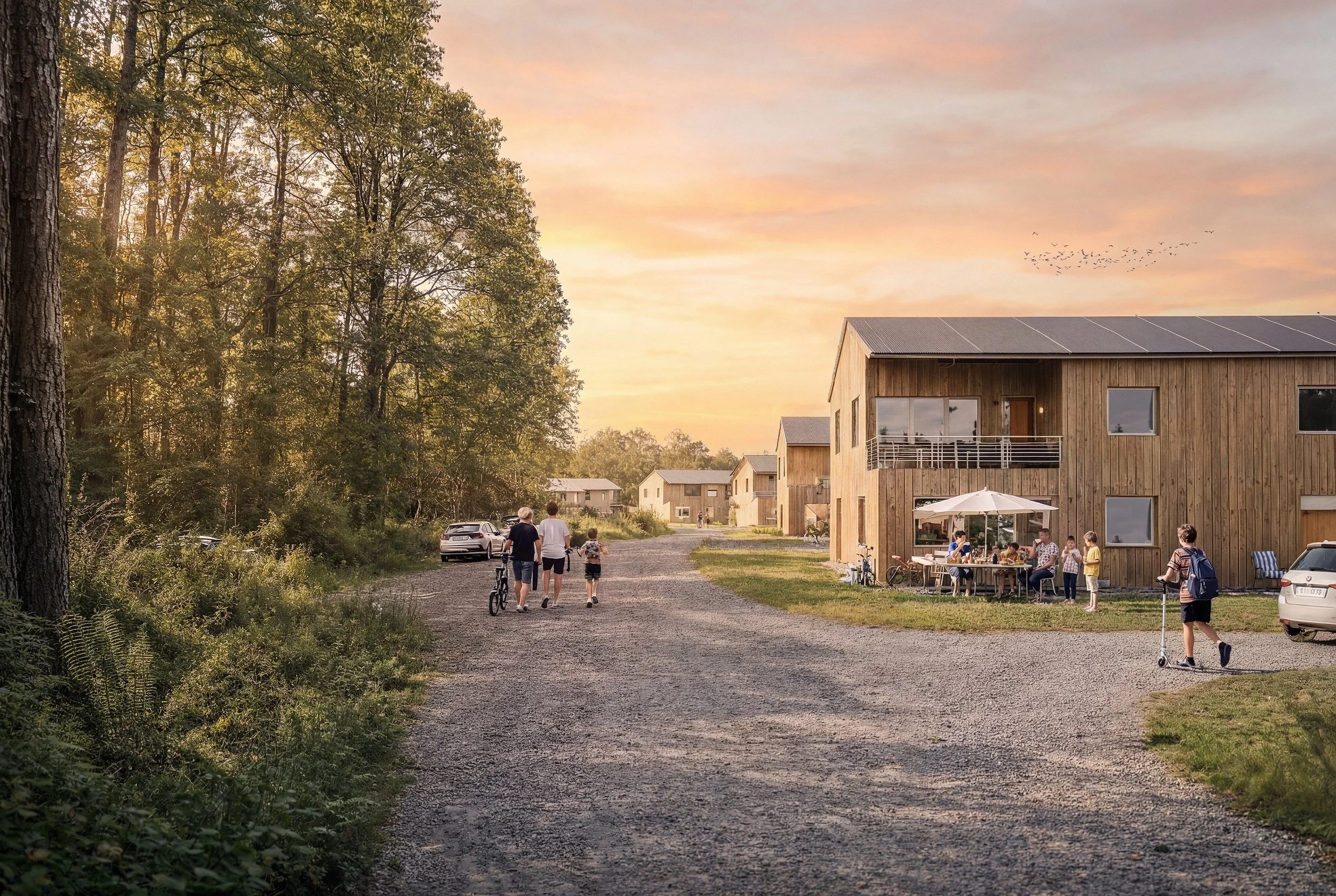 Familj promenerar och leker utanför moderna trähus under solnedgång i landsbygdsområde.