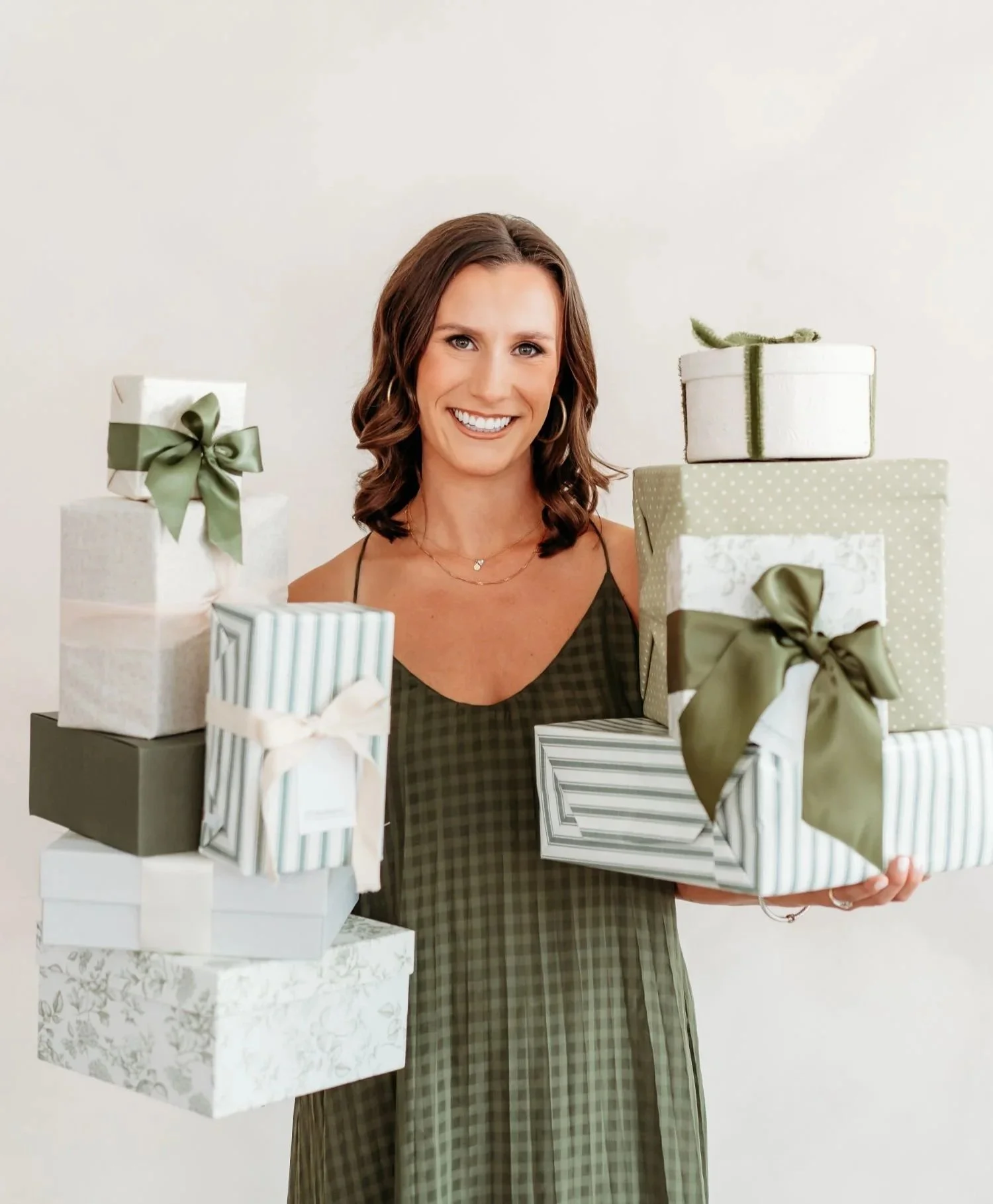 Smiling woman holding elegantly wrapped gifts with green bows.