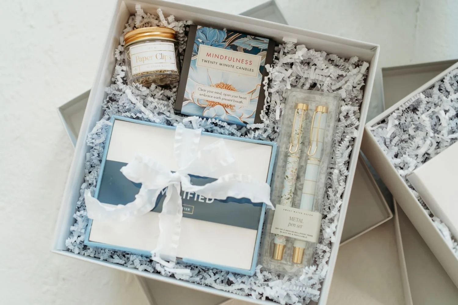 Gift box with shredded paper contains a candle, pens, a small bottle and more.
