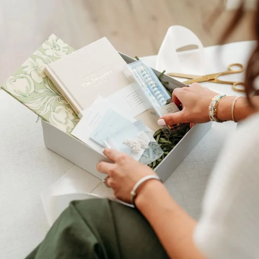 A woman arranges decorative paper, scissors, and a box on a table.