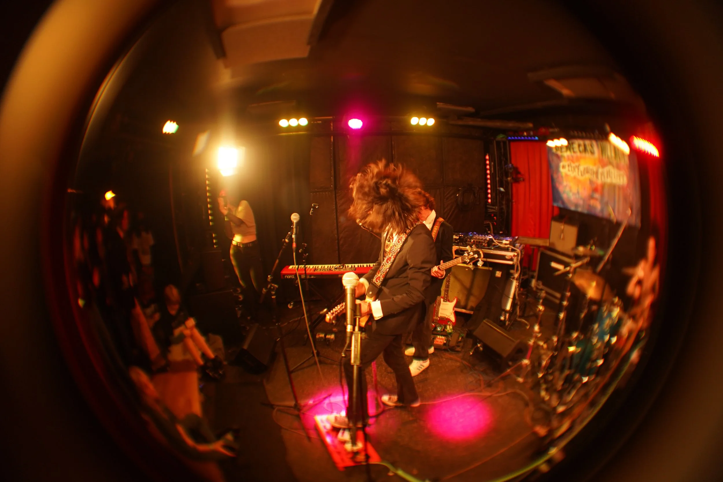 Musicians performing on stage with vibrant lighting and a crowd in the audience.
