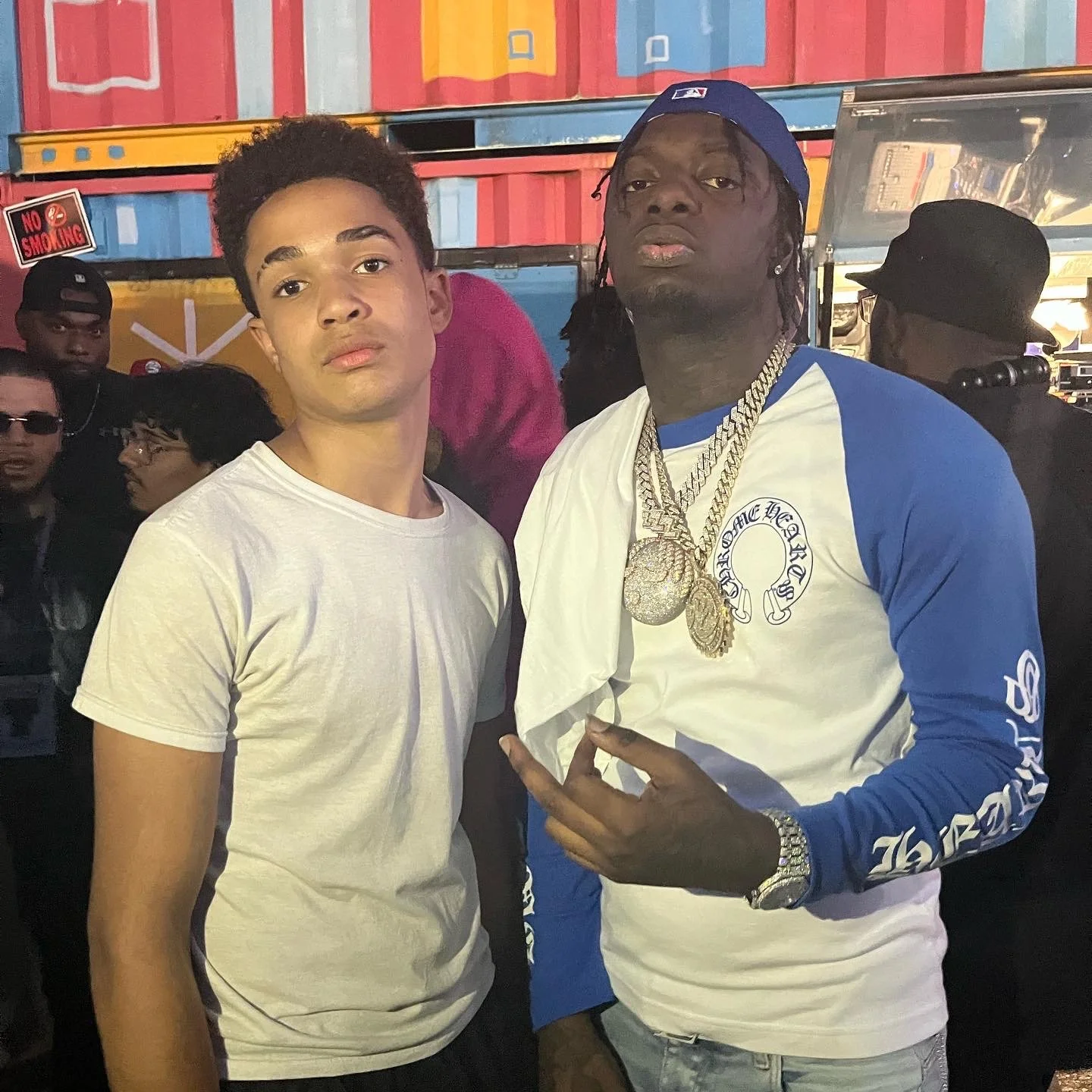 Two men standing side by side in a busy, colorful setting with other people in the background.