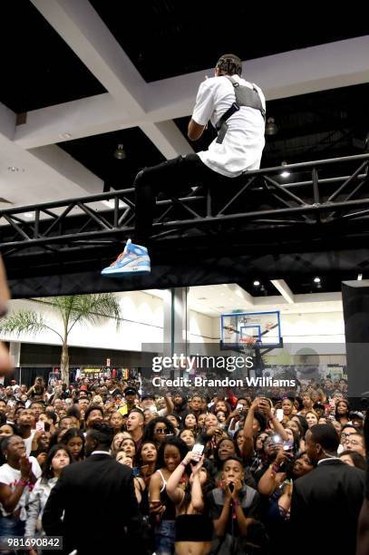 A man sitting on a metal platform above a crowd of people in an indoor venue, with some individuals taking photos and a basketball hoop in the background.