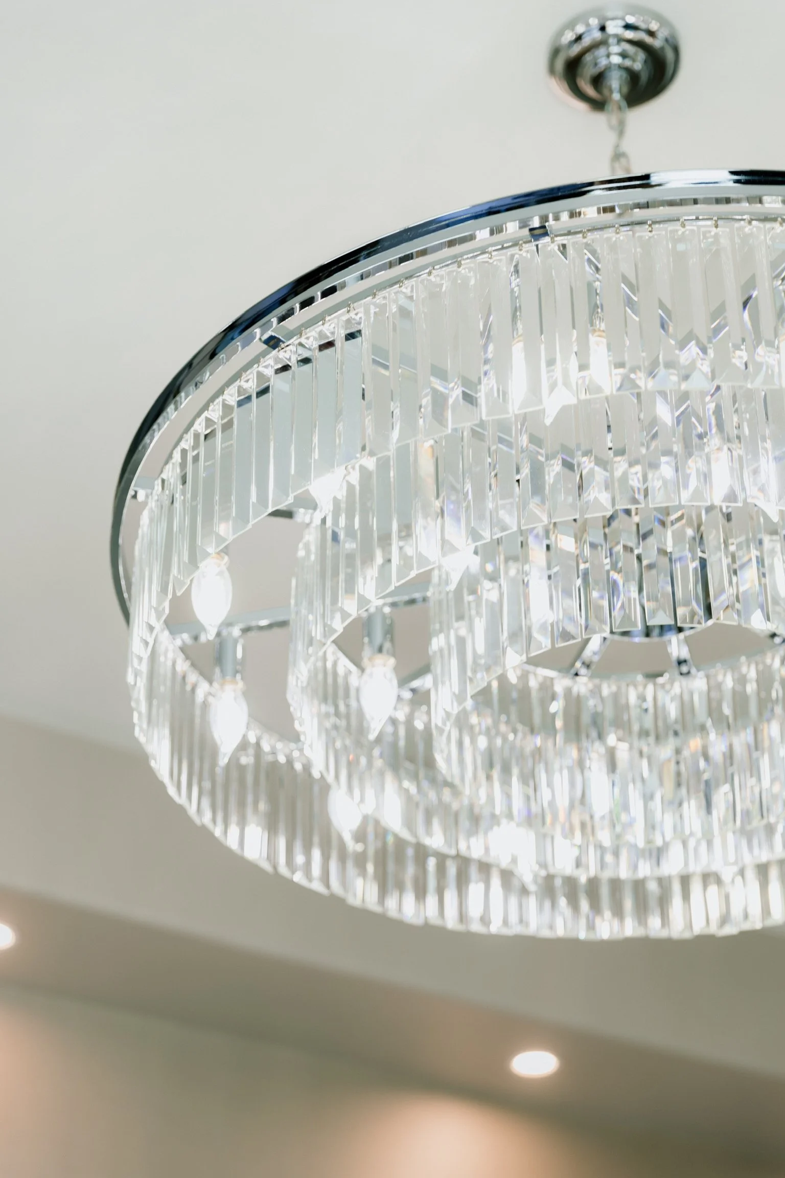 Close-up of a modern, circular crystal chandelier hanging from the ceiling.