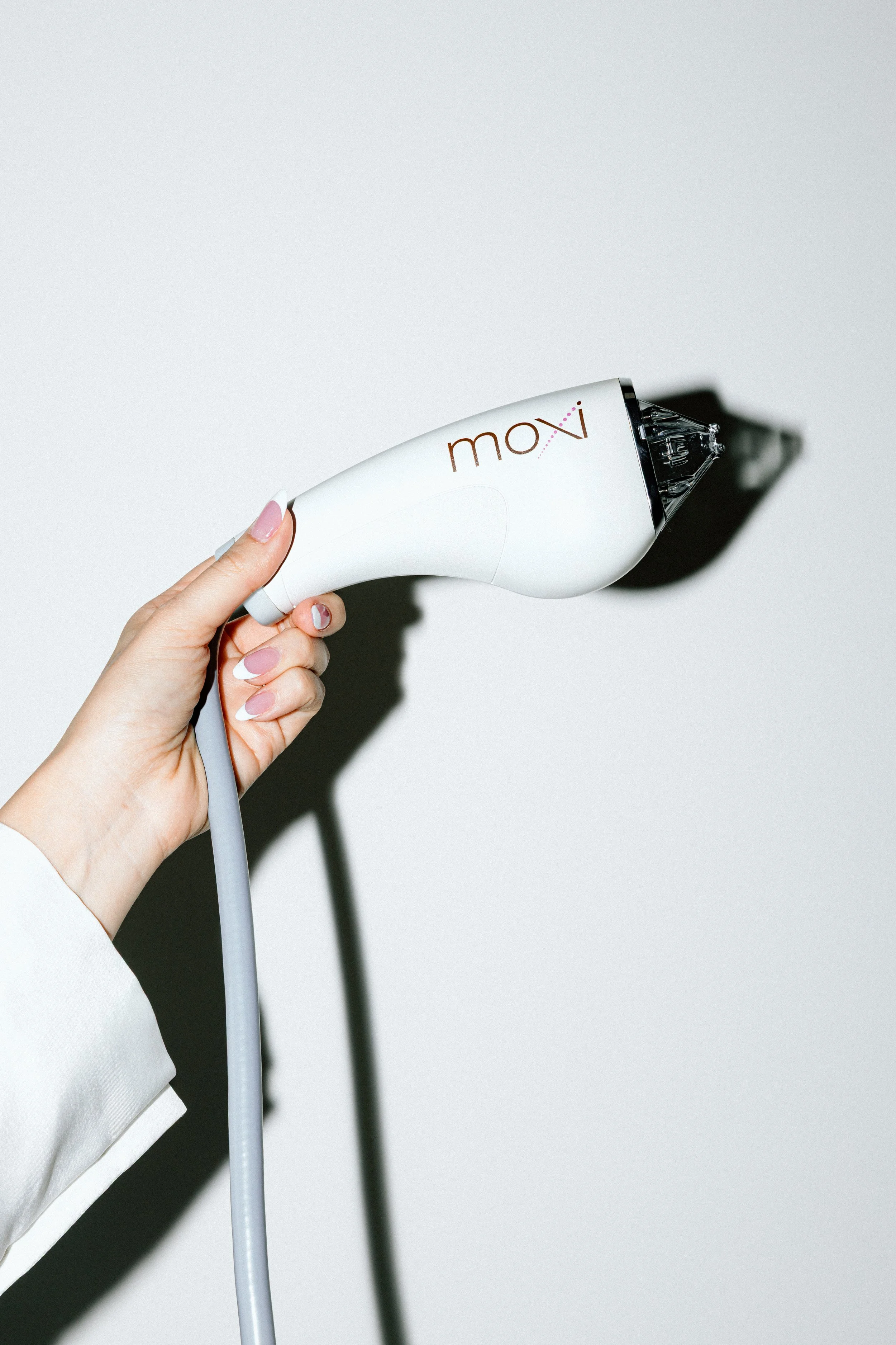 A hand holding a white small device with the word "moxi" printed on it, casting a shadow on a plain white background.