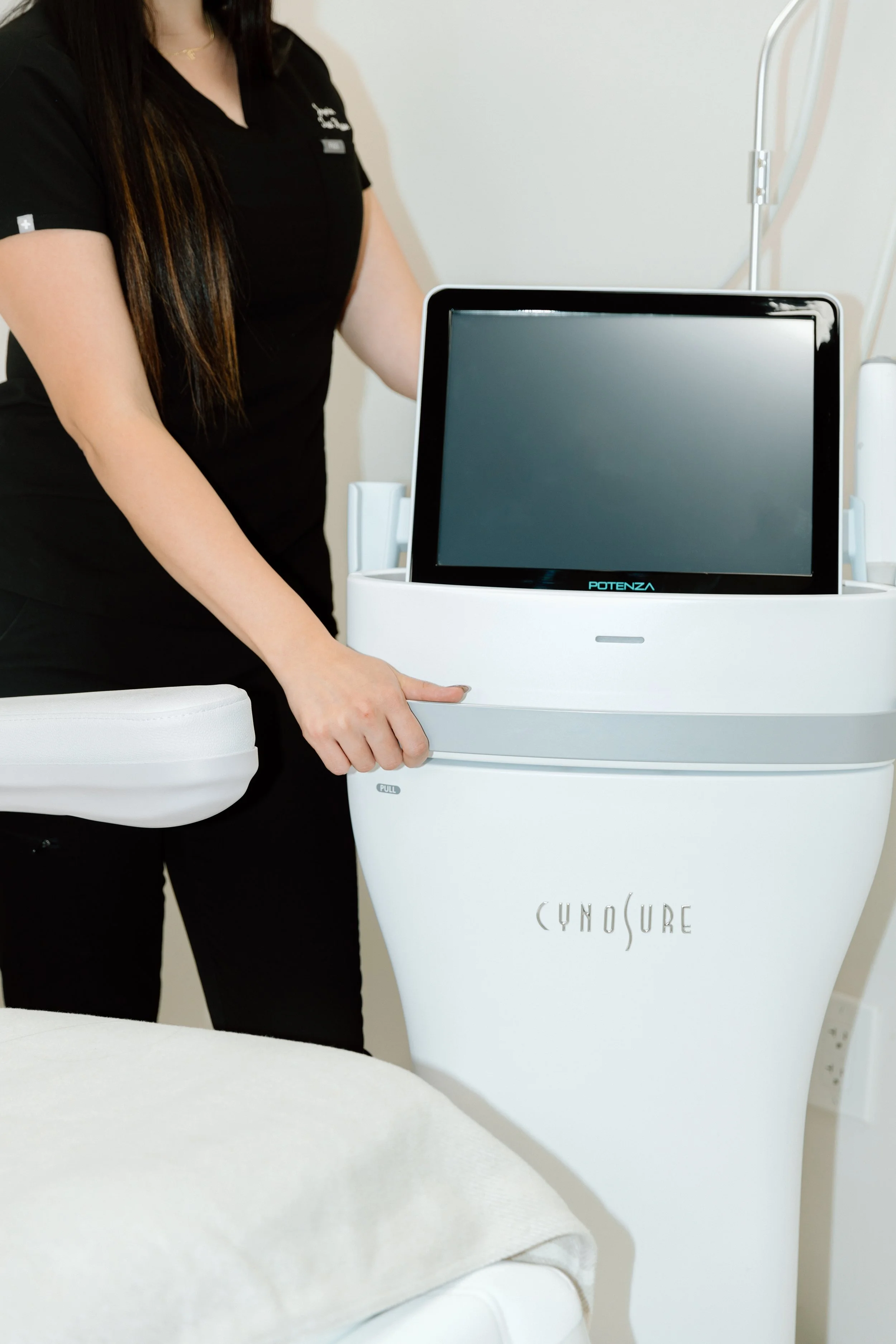A healthcare professional standing next to a CynoSure medical device with a large screen, in a clinical setting.