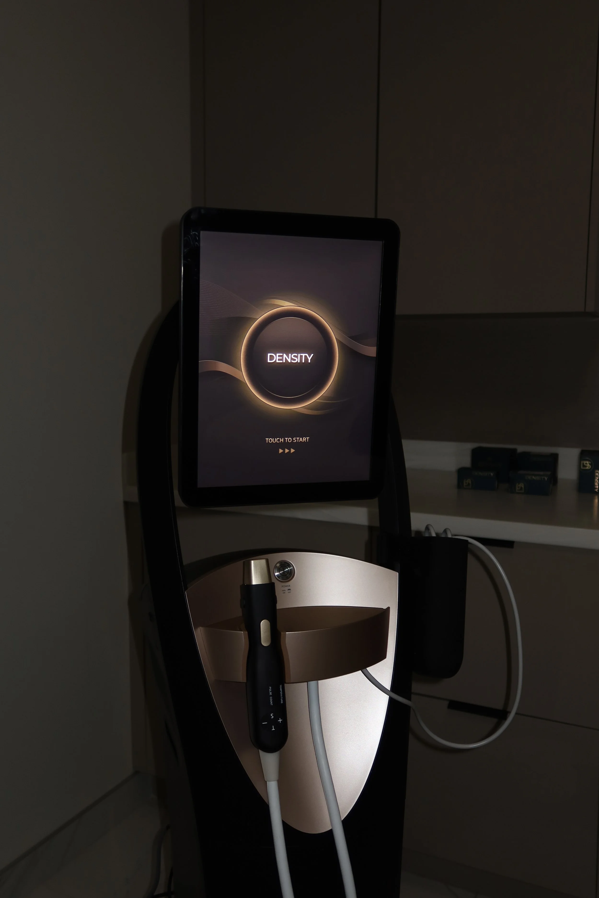 An electronic device for skin rejuvenation with a touch screen displaying the word 'DENSITY' and a circular graphic, with cords and a stylus pen in the lower part of the image.
