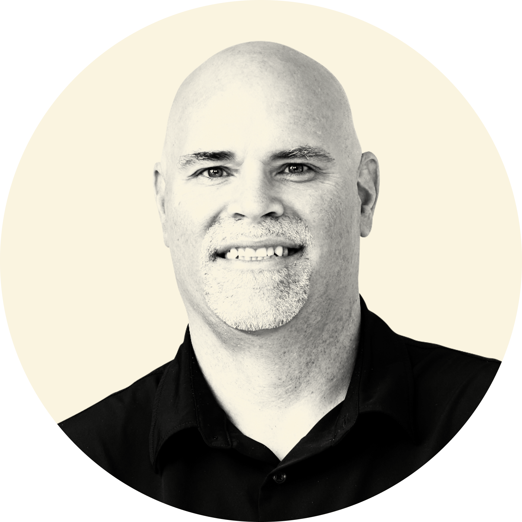 Black and white portrait photograph of a smiling bald man with a goatee, wearing a dark shirt.