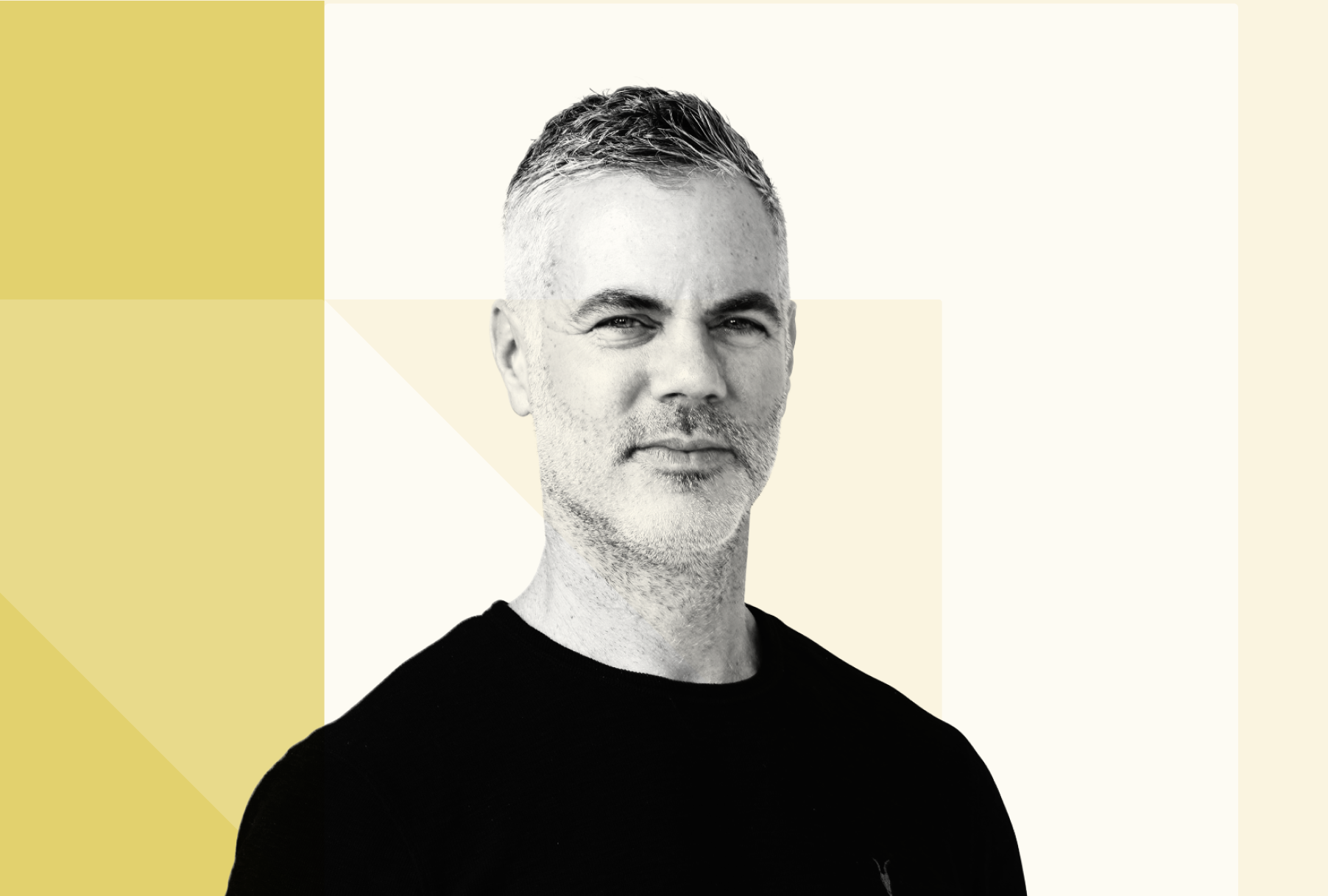 Black and white portrait of Stephen Fogarty with short, light-colored hair and a beard, wearing a black shirt, against a geometric background in shades of beige and white.