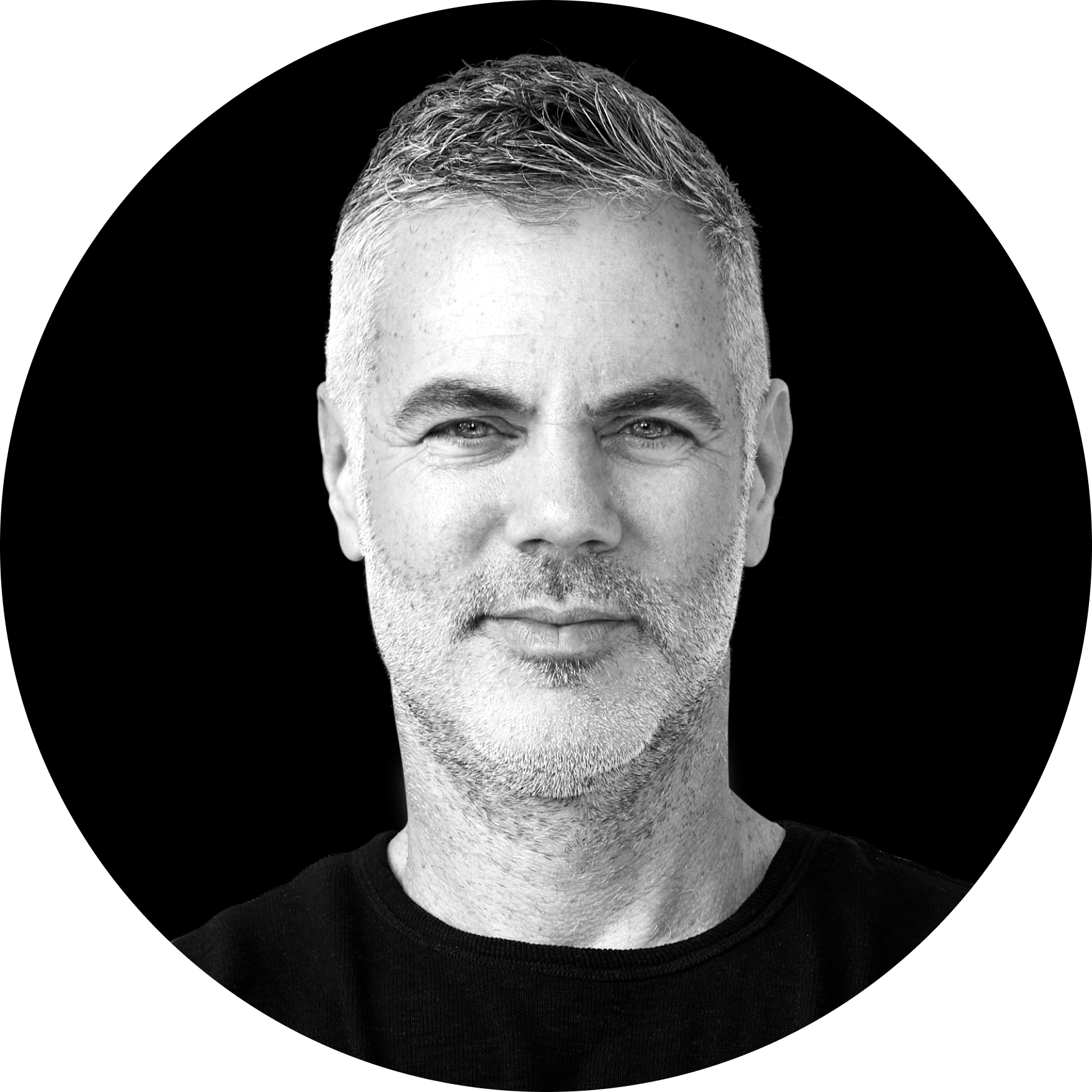 Black and white portrait of Stephen Fogarty with short hair and a beard, smiling slightly, against a black background.
