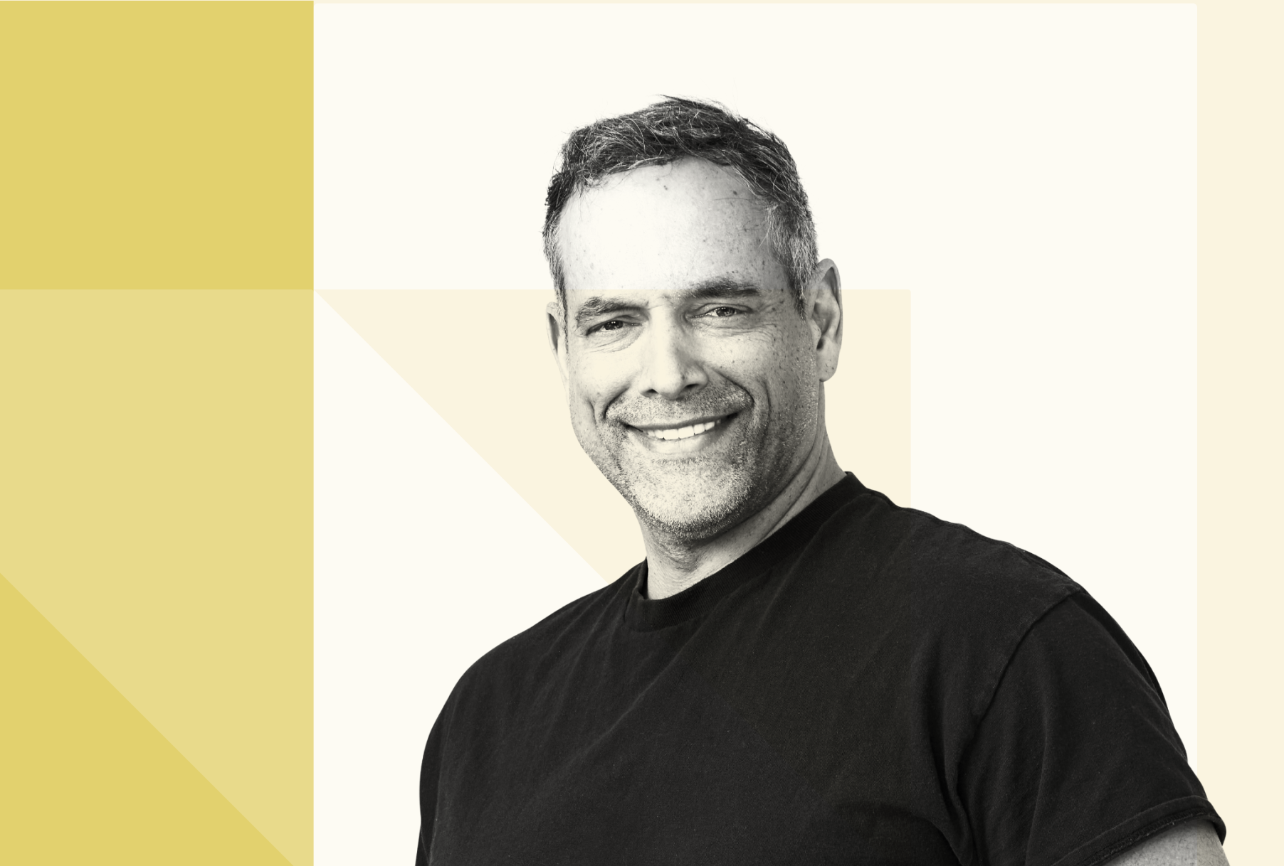 Black-and-white portrait of Mike Bajda with short hair, wearing a black t-shirt, standing against a light background with partial yellow geometric design.